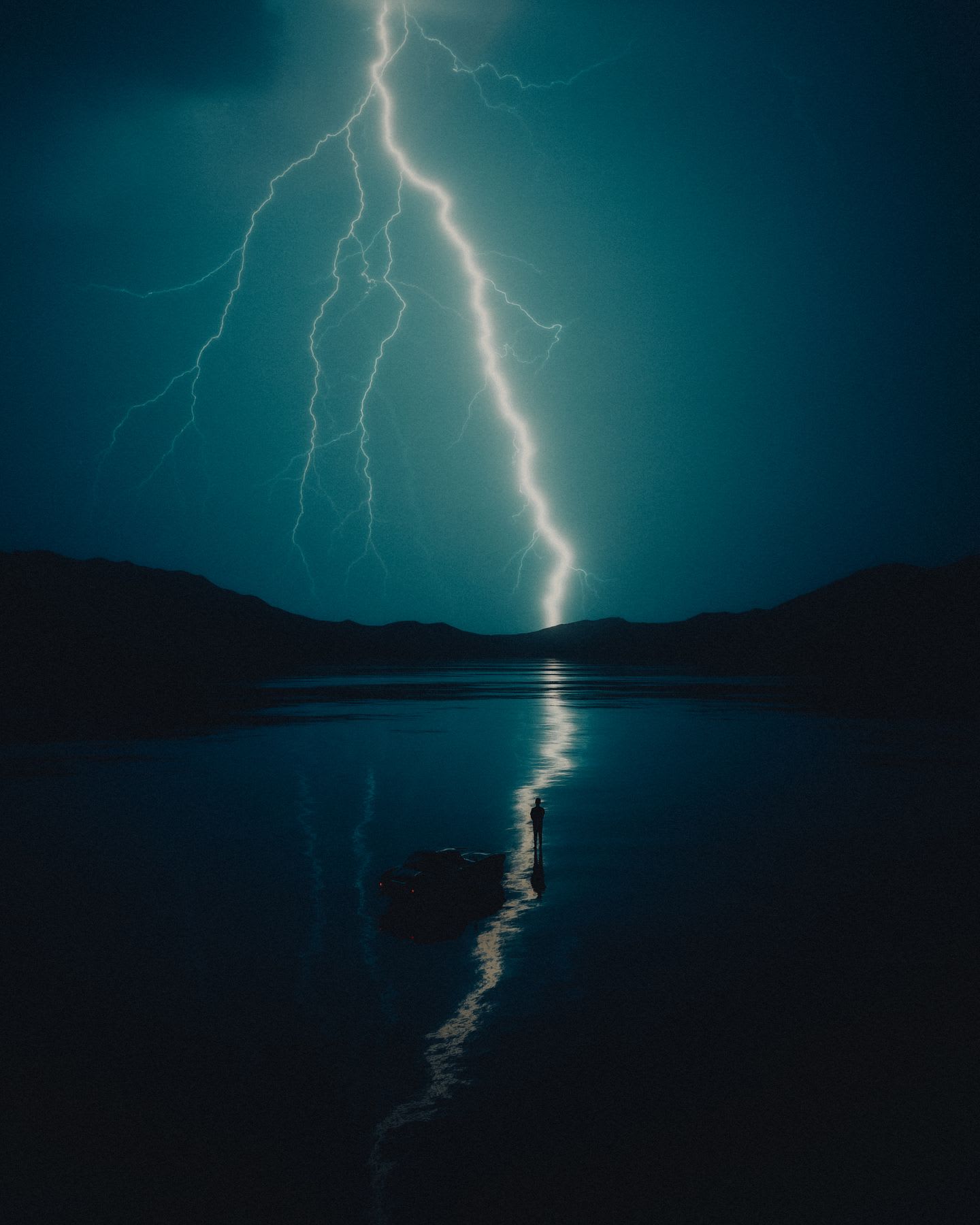 A person standing next to a car on a lake, under a thunderstorm with lightning illuminating the night sky.