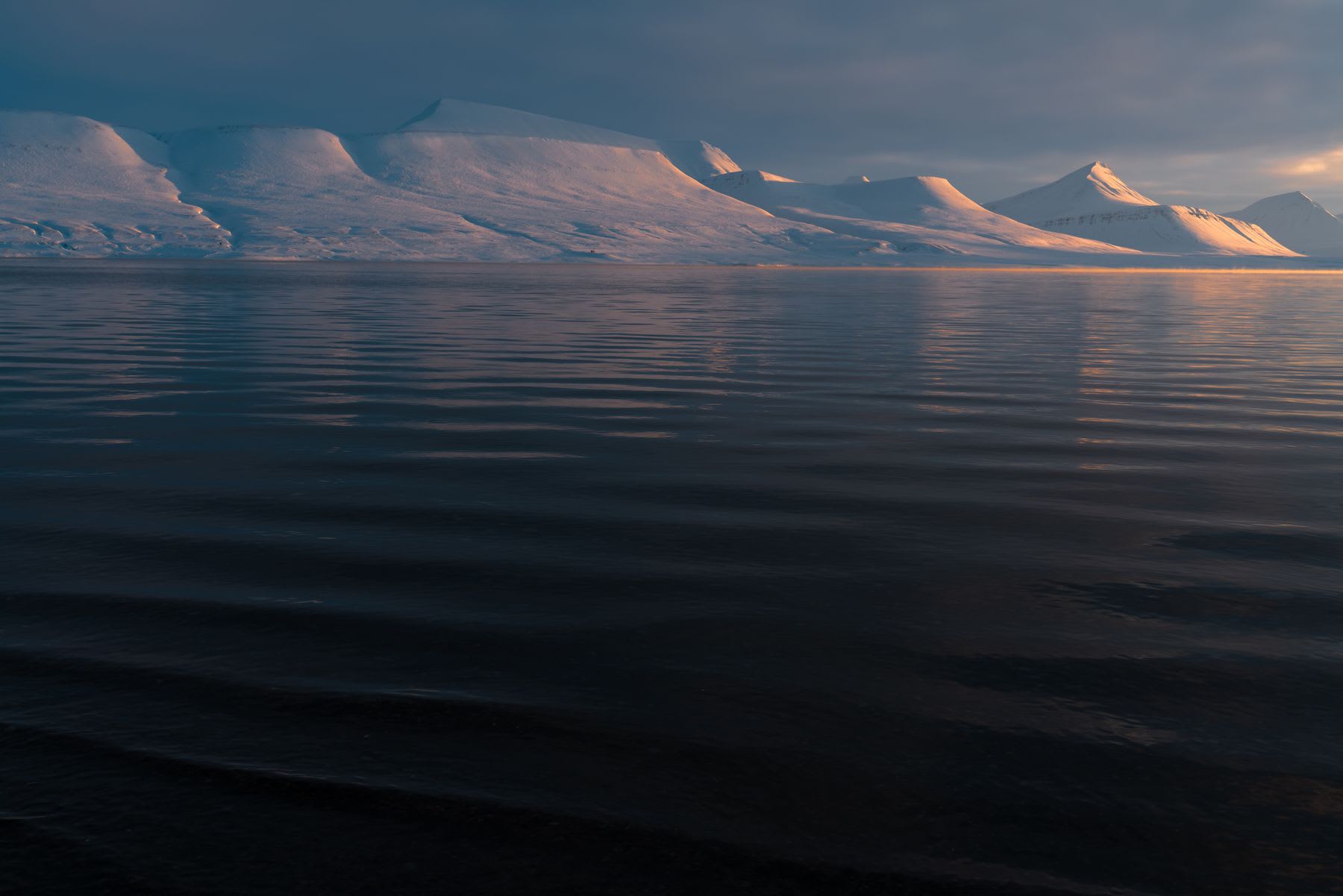 Snow-covered mountains reflected in calm waters at dusk.