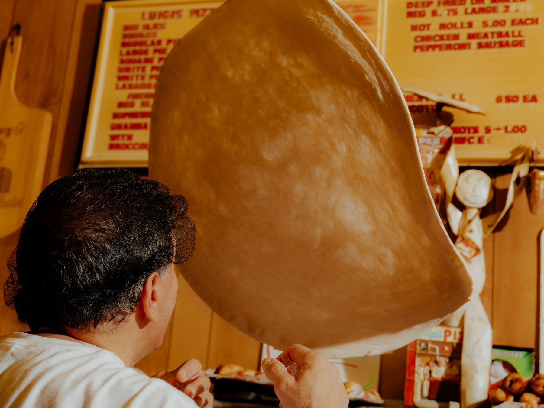 A man wearing a black cap is throwing a pizza dough up