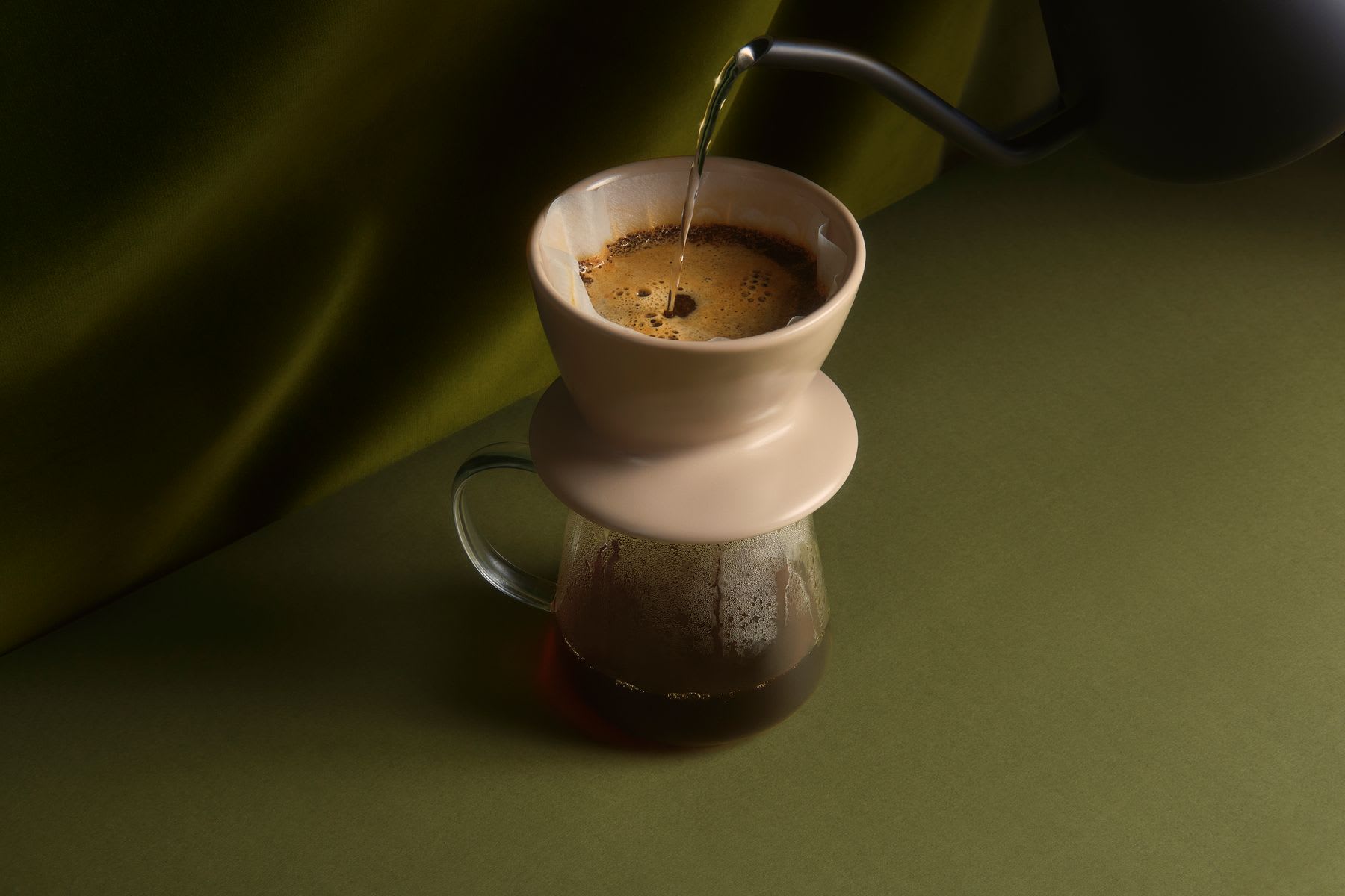 Hot water is poured from a gooseneck kettle into a ceramic dripper to brew pour-over coffee into a glass server.