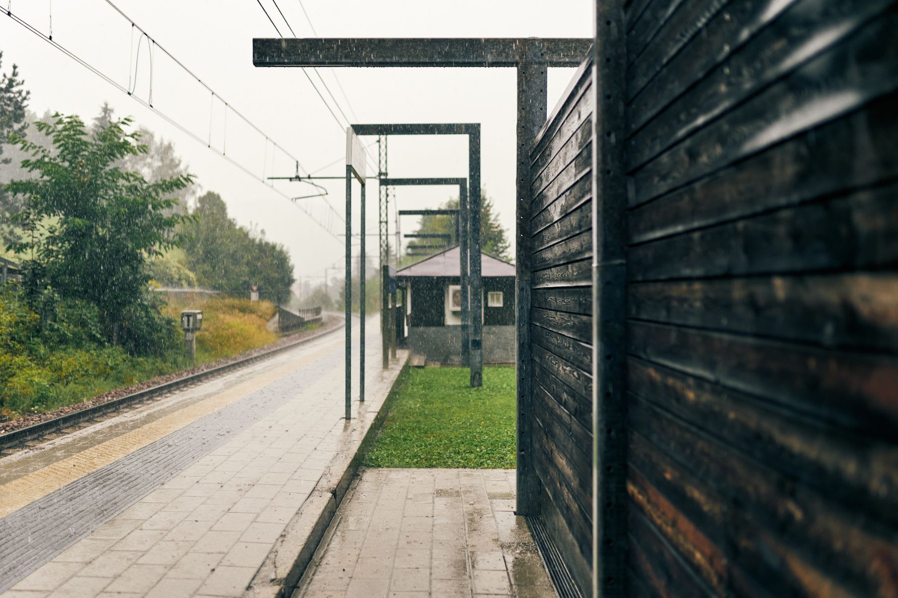 Under a rainy sky, a small building is located next to the landing of a small outdoor train station.