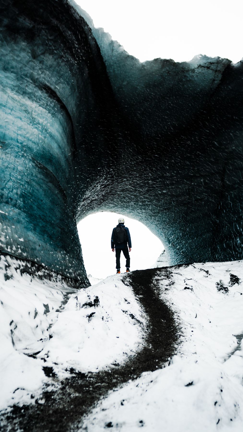 Person standing under an ice arch with bluish walls.