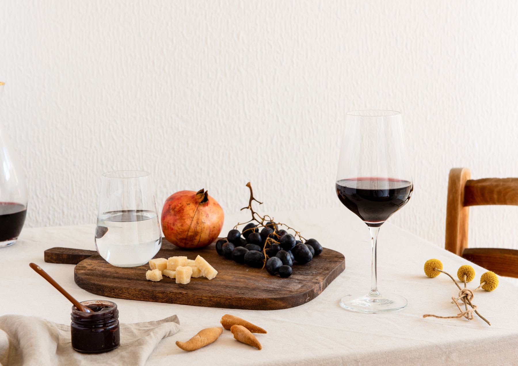 A still life of a table with wine, grapes, cheese, and a pomegranate.