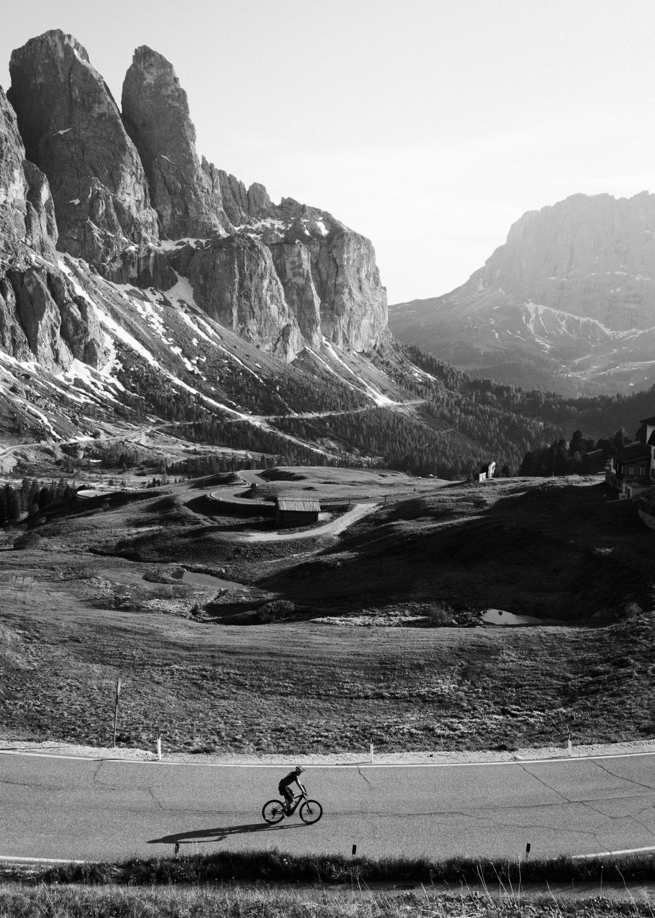 A cyclist rides a bicycle on a rural highway in a mountainous area.