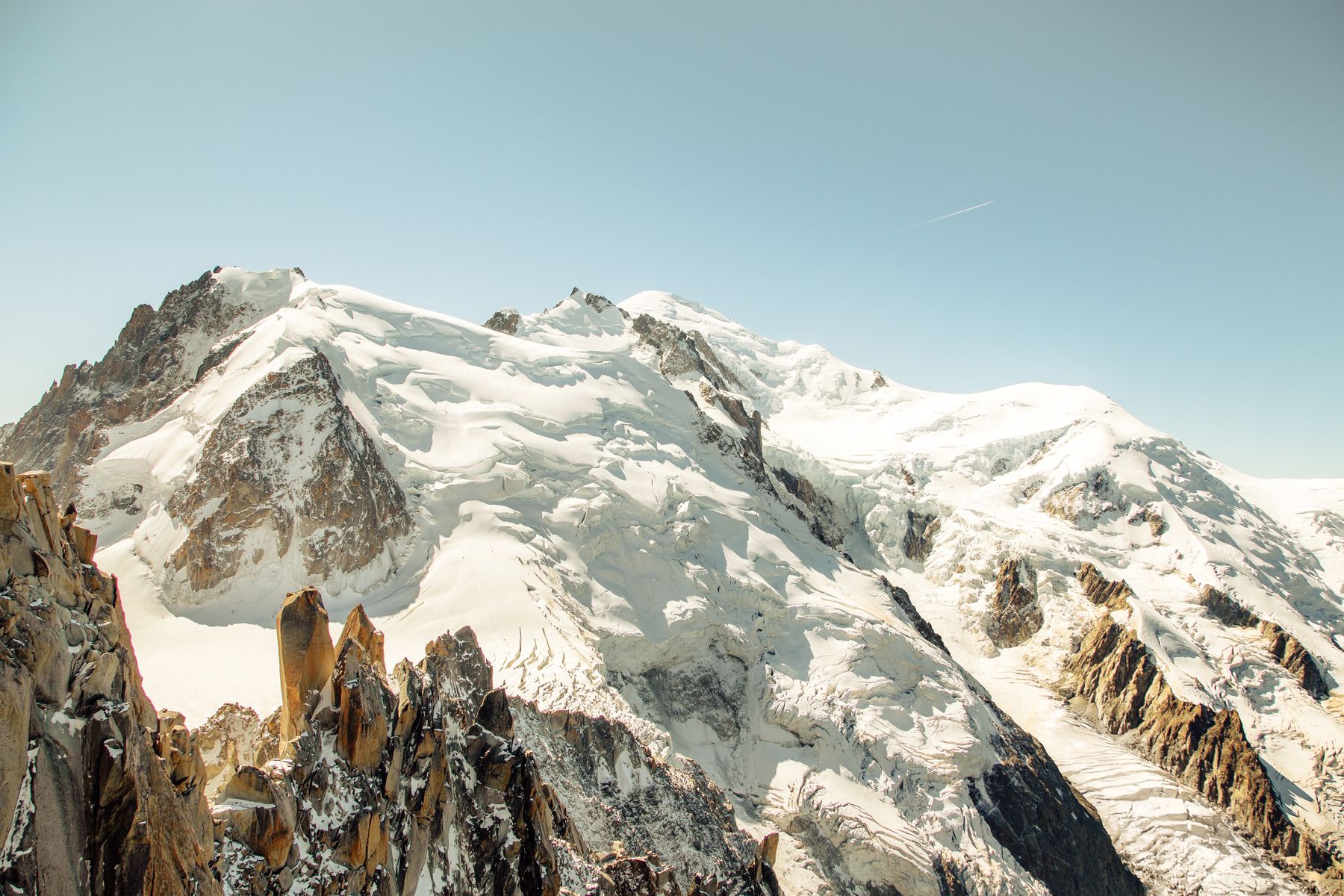 Snow-covered mountain peaks under a clear blue sky, with rugged rocky ridges in the foreground.