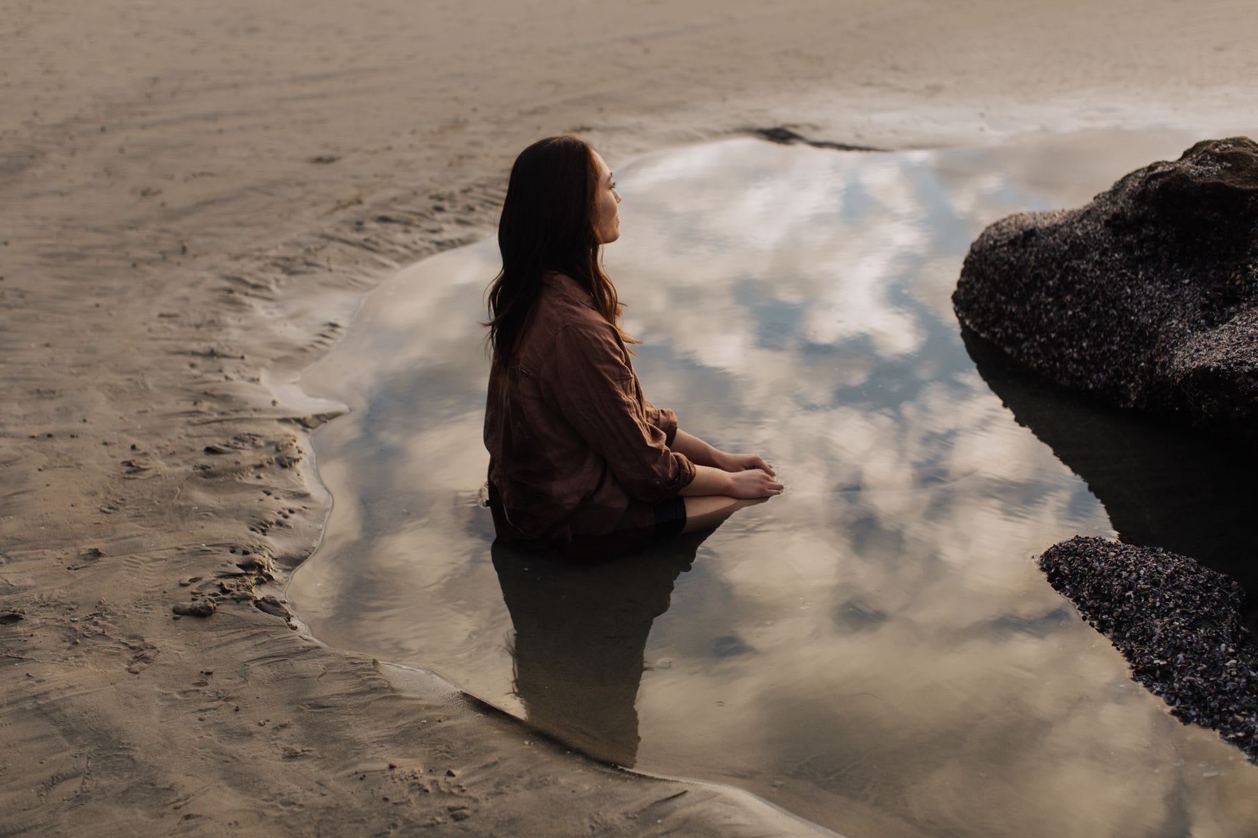 Woman sits in reflective tidal pool on the beach.