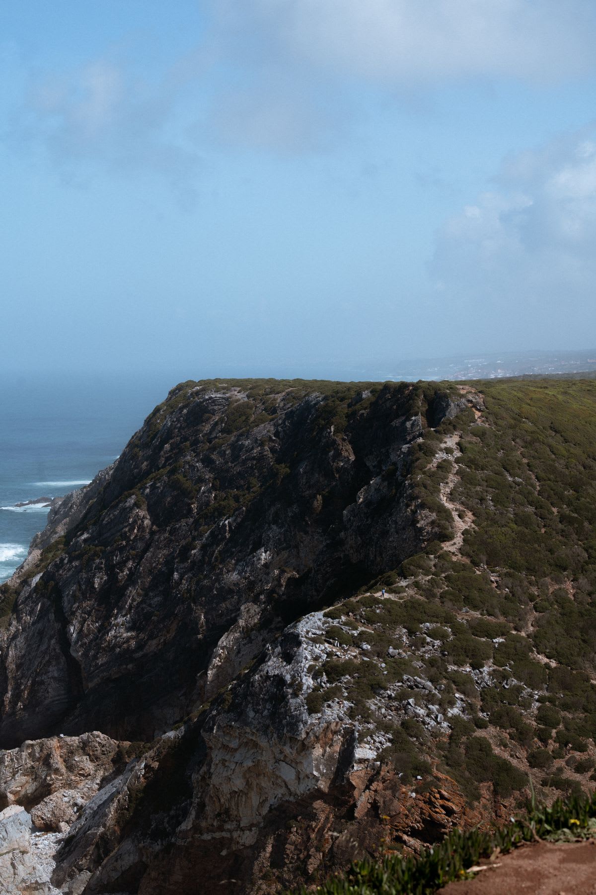 A rocky cliff overlooking the ocean under a partly cloudy sky