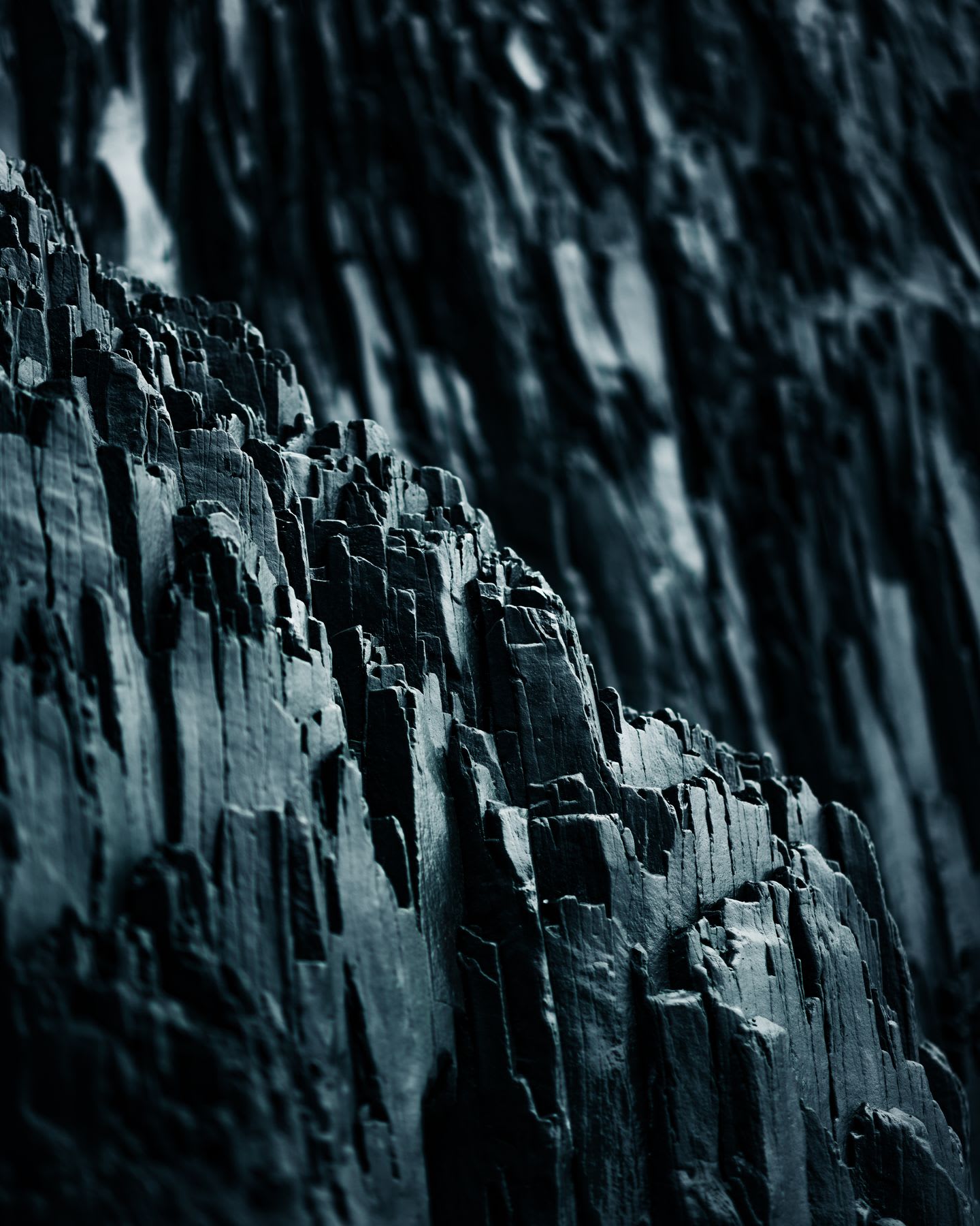 A dramatic close-up of a jagged, dark grey geological formation with a moody, shallow focus.