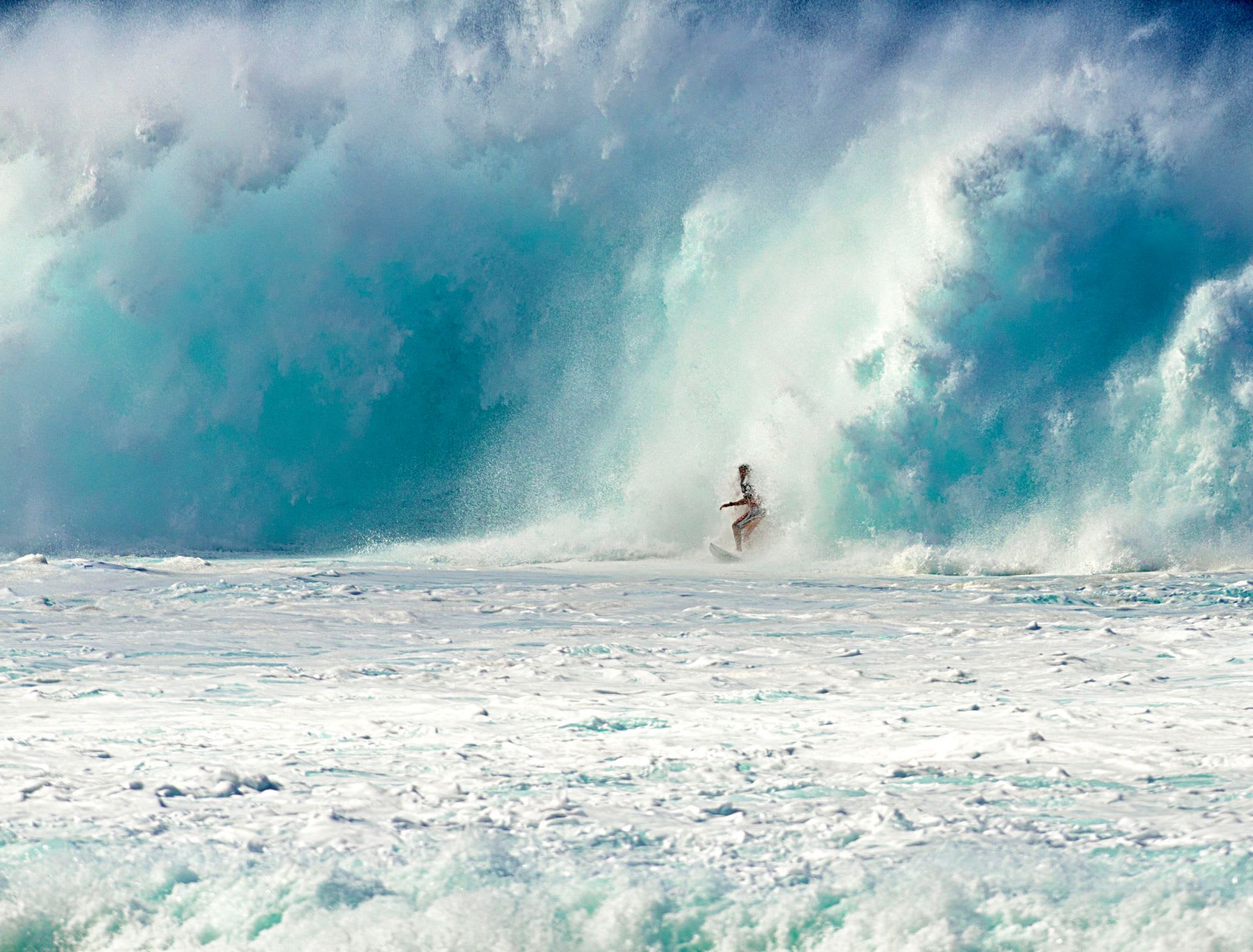 A surfer rides a massive wave in the ocean with water crashing around.
