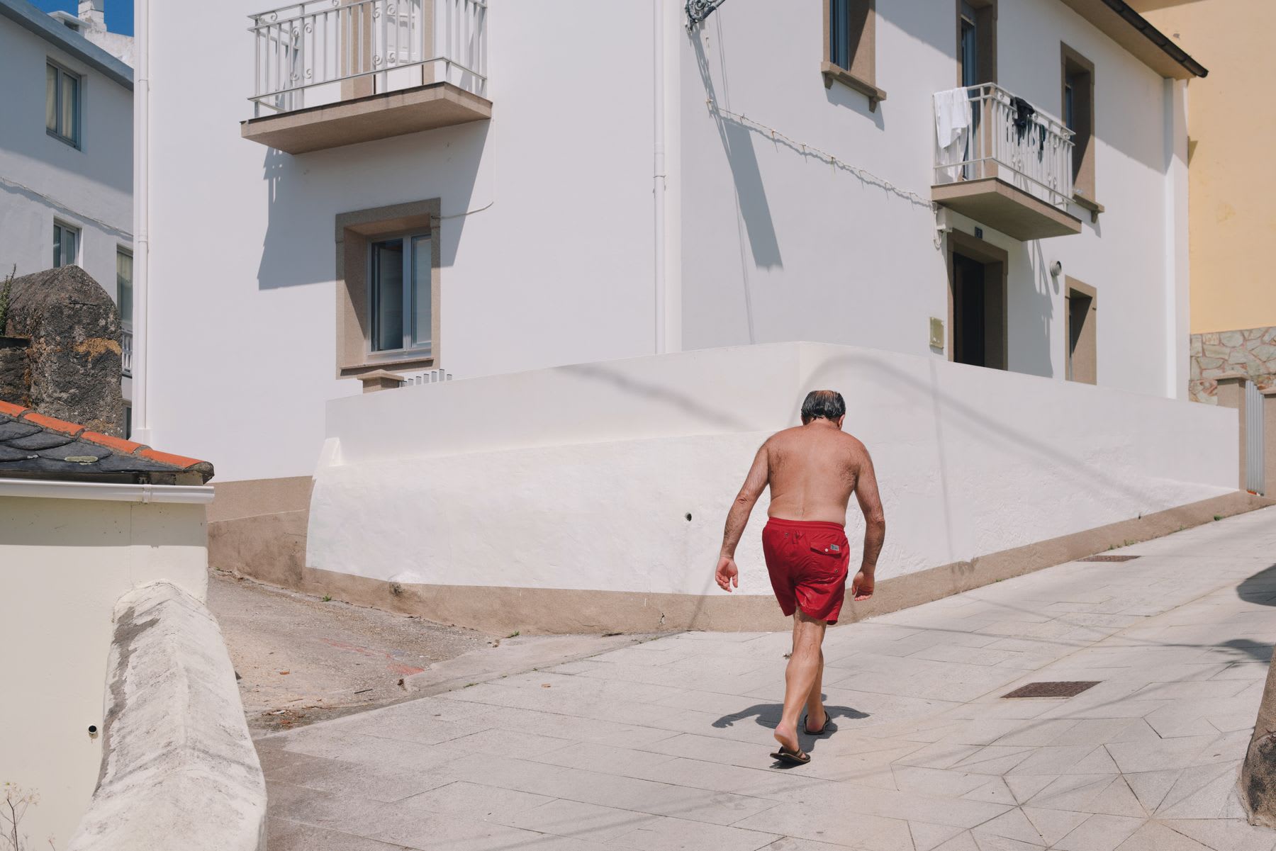 Man without a t-shirt and in red shorts walking through a residential neighborhood