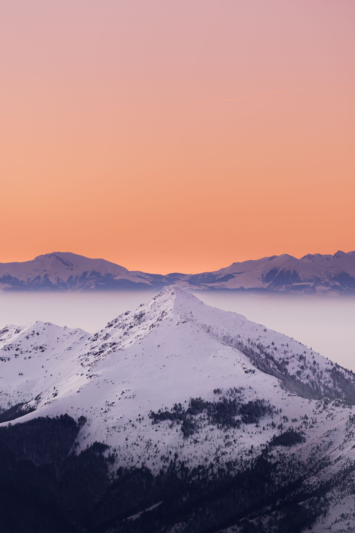 Snow covered mountains high in the clouds under an orange sky