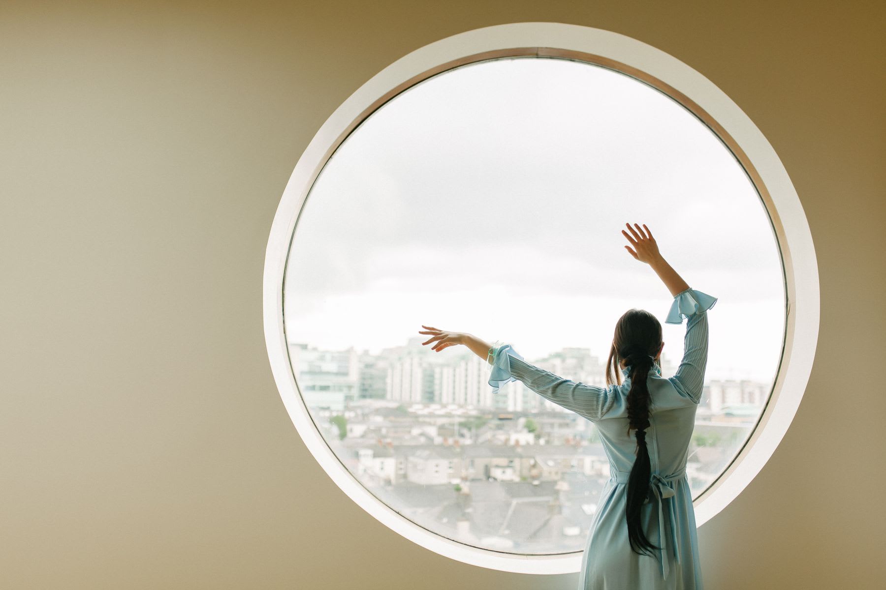 Woman dancing in front of a round window with a view of the neighborhood