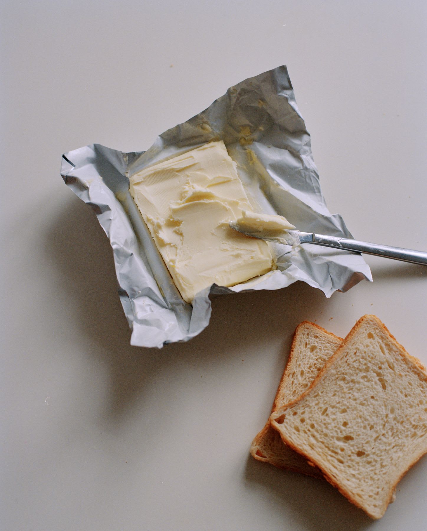 Block of butter with a knife next to two slices of bread.
