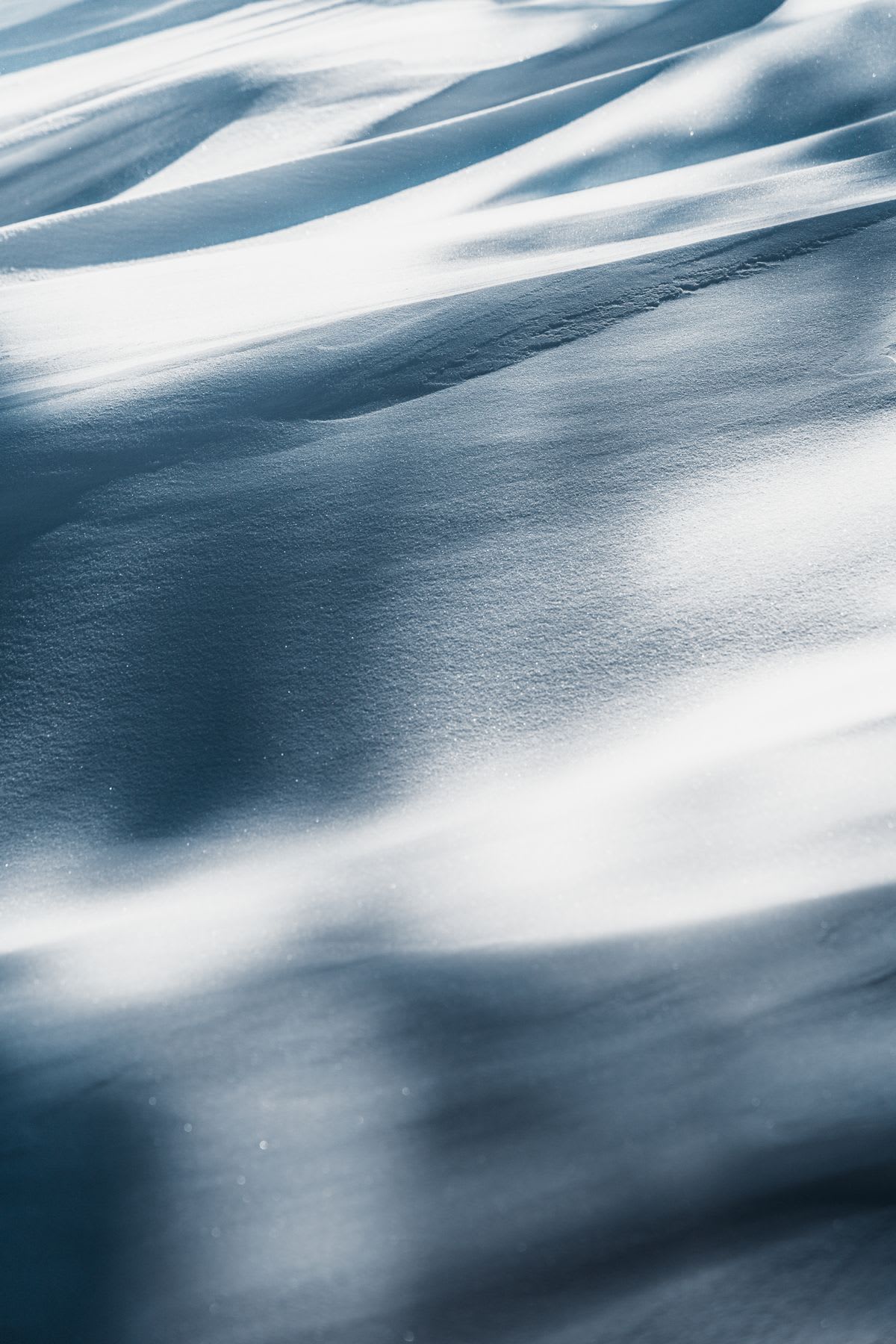 Close-up of smooth snowdrifts with subtle shadows, capturing the texture and contours of the snow in soft light.