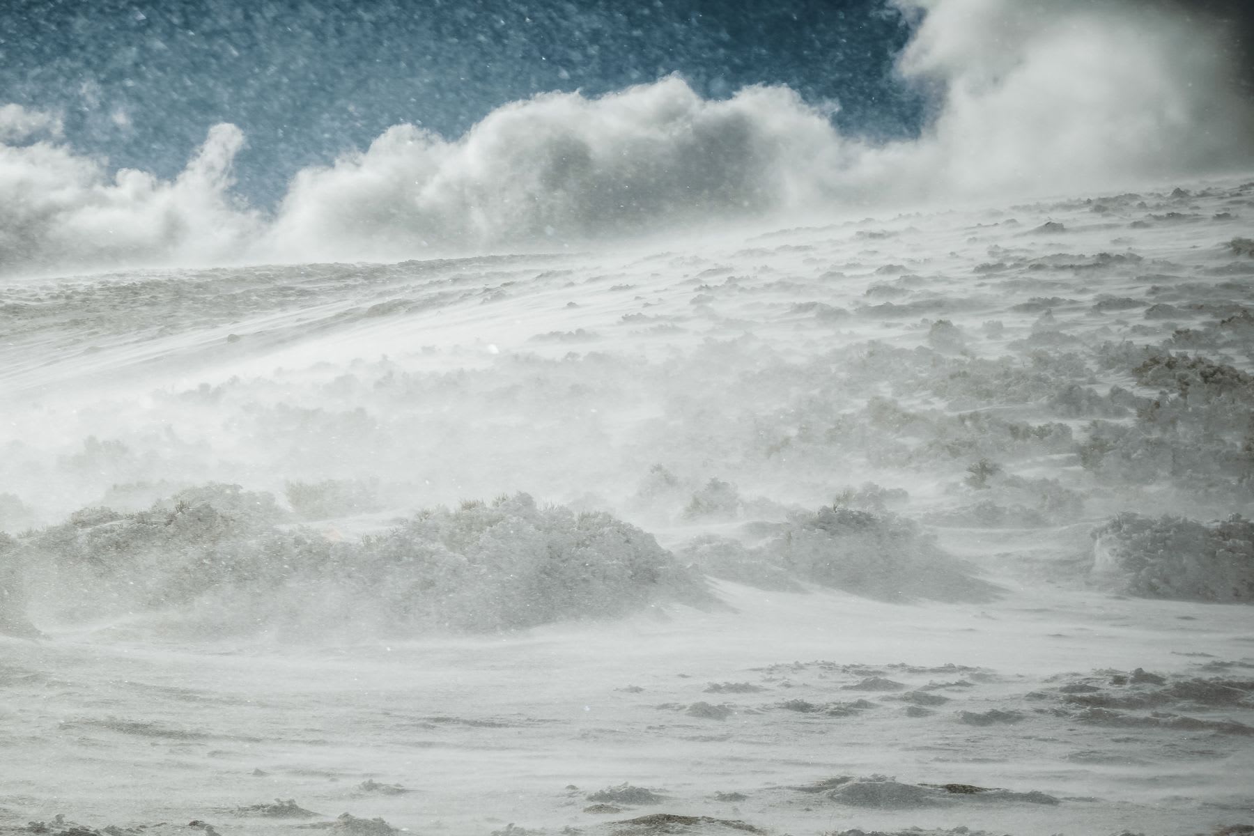 A fierce blizzard with high winds sweeps across a snow-covered mountain landscape.