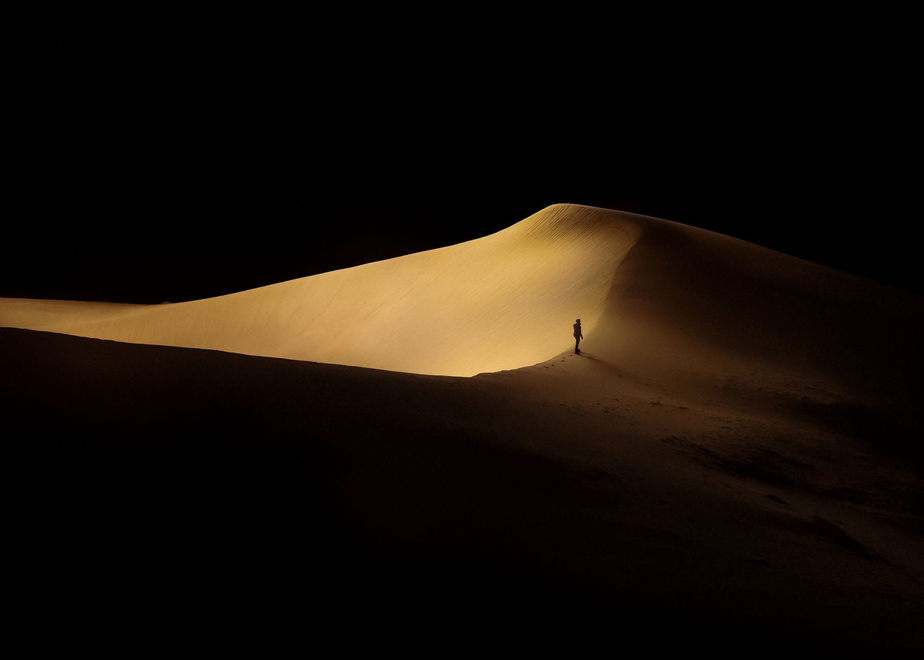A man walking the crest of a sand dune at night.