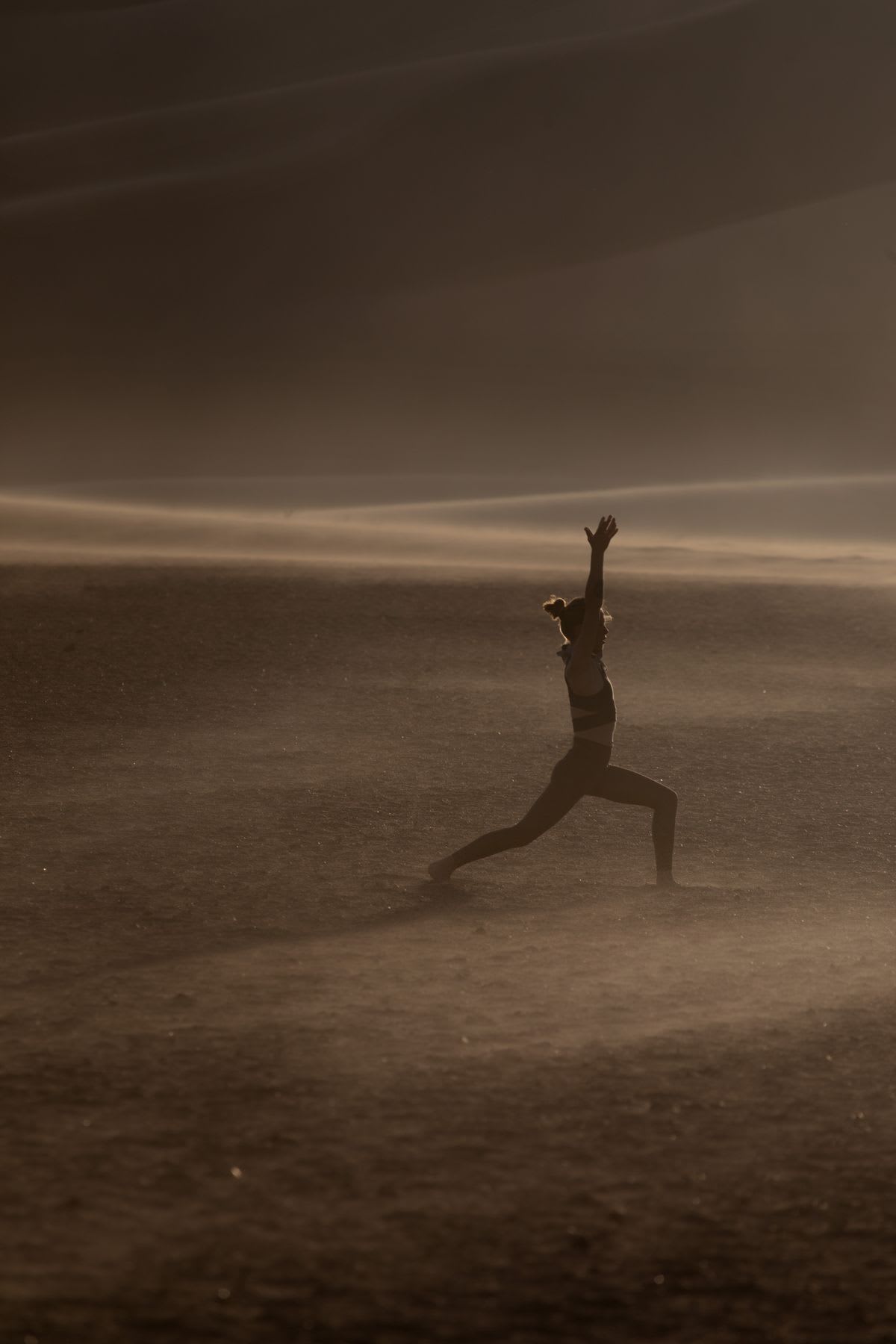 A woman is in a sandy region with dunes and she is stretching her leg