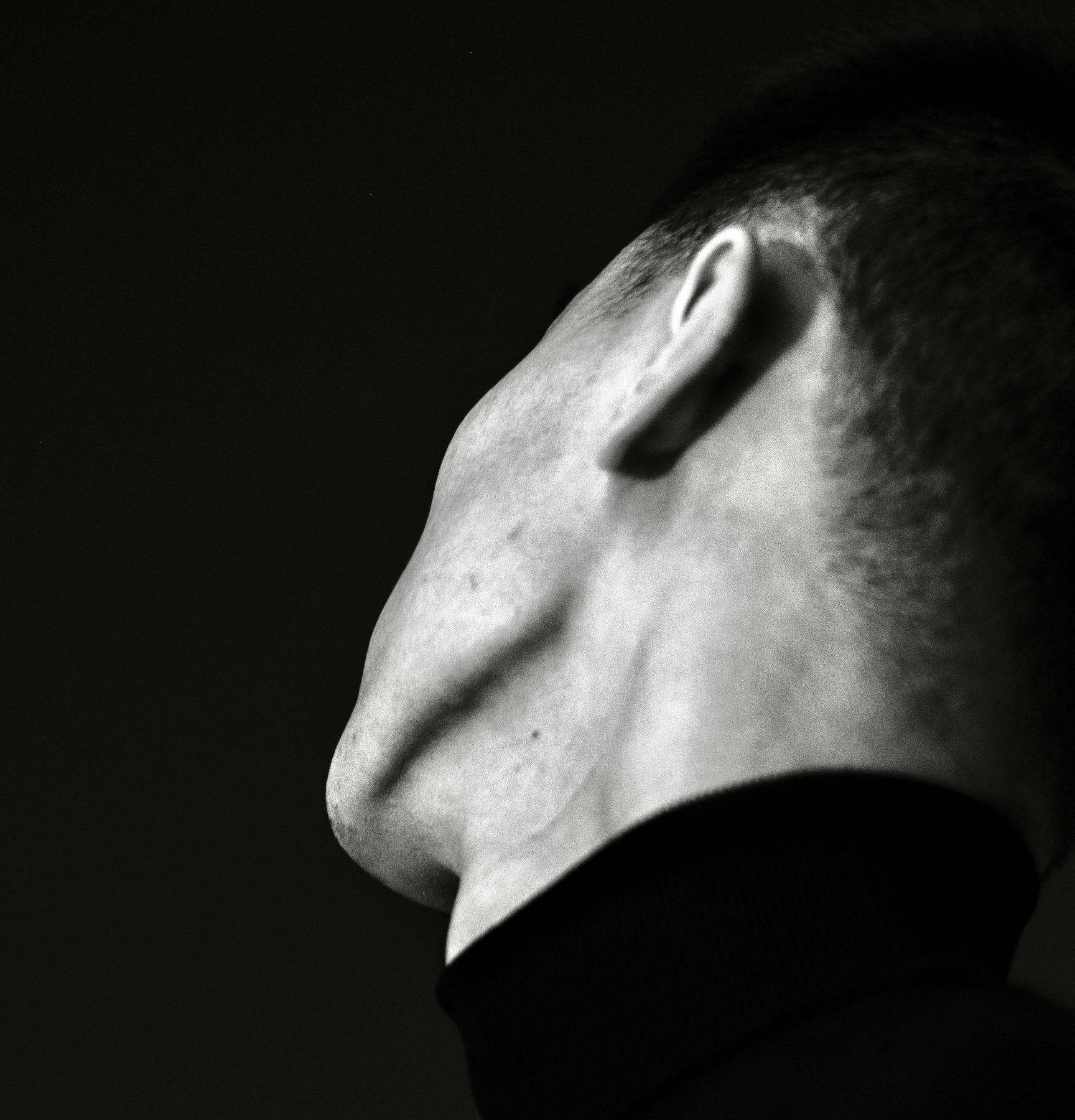 Black and white portrait of a male with a neutral expression taken indoors with low key lighting