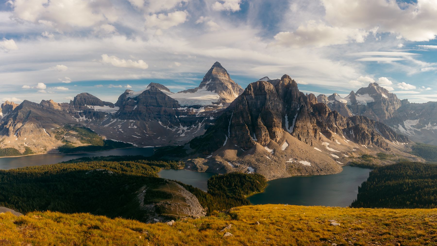 Landscape of mountain ranges with snowy cliffs surrounded by a lake on a blue sky day with clouds