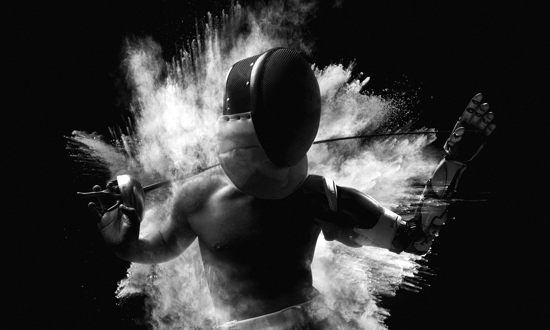 A person wearing a mask and fencing gloves is surrounded by an explosion of dust.