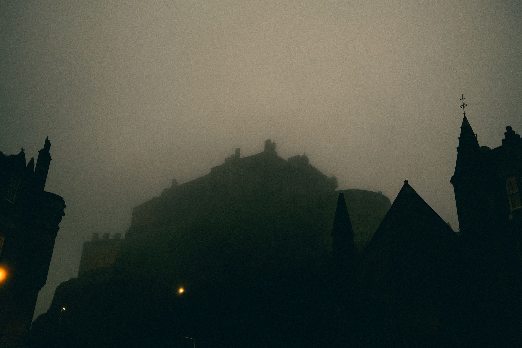The dark silhouettes of a historic castle and surrounding buildings are enveloped in thick, atmospheric fog at night.