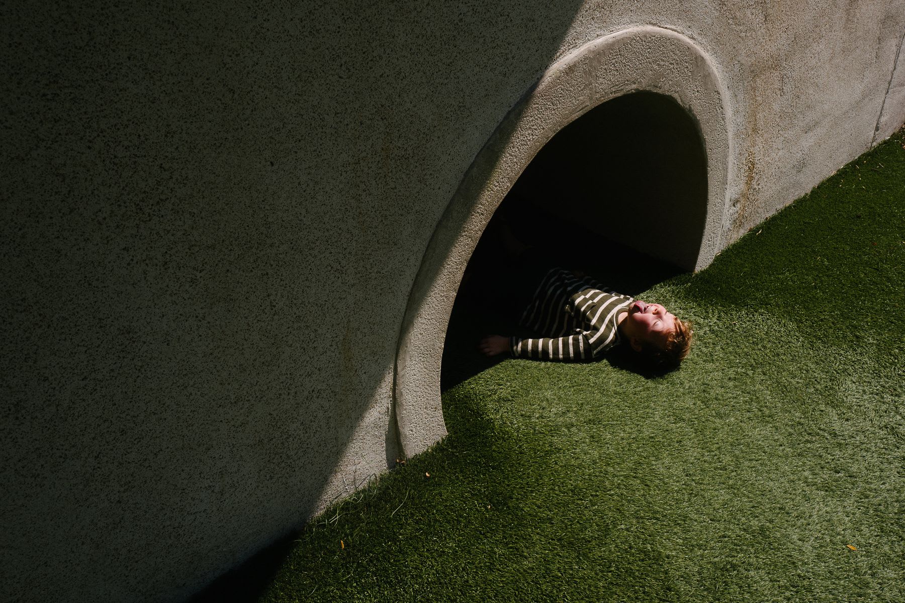 Young boy sticks out his tongue while lying half way in a tunnel passing through a building.