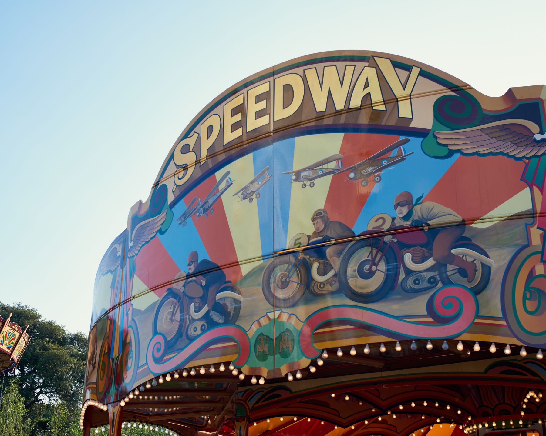 Decorative mural on a carousel depicting racing motorcyclists under the sign "SPEEDWAY".