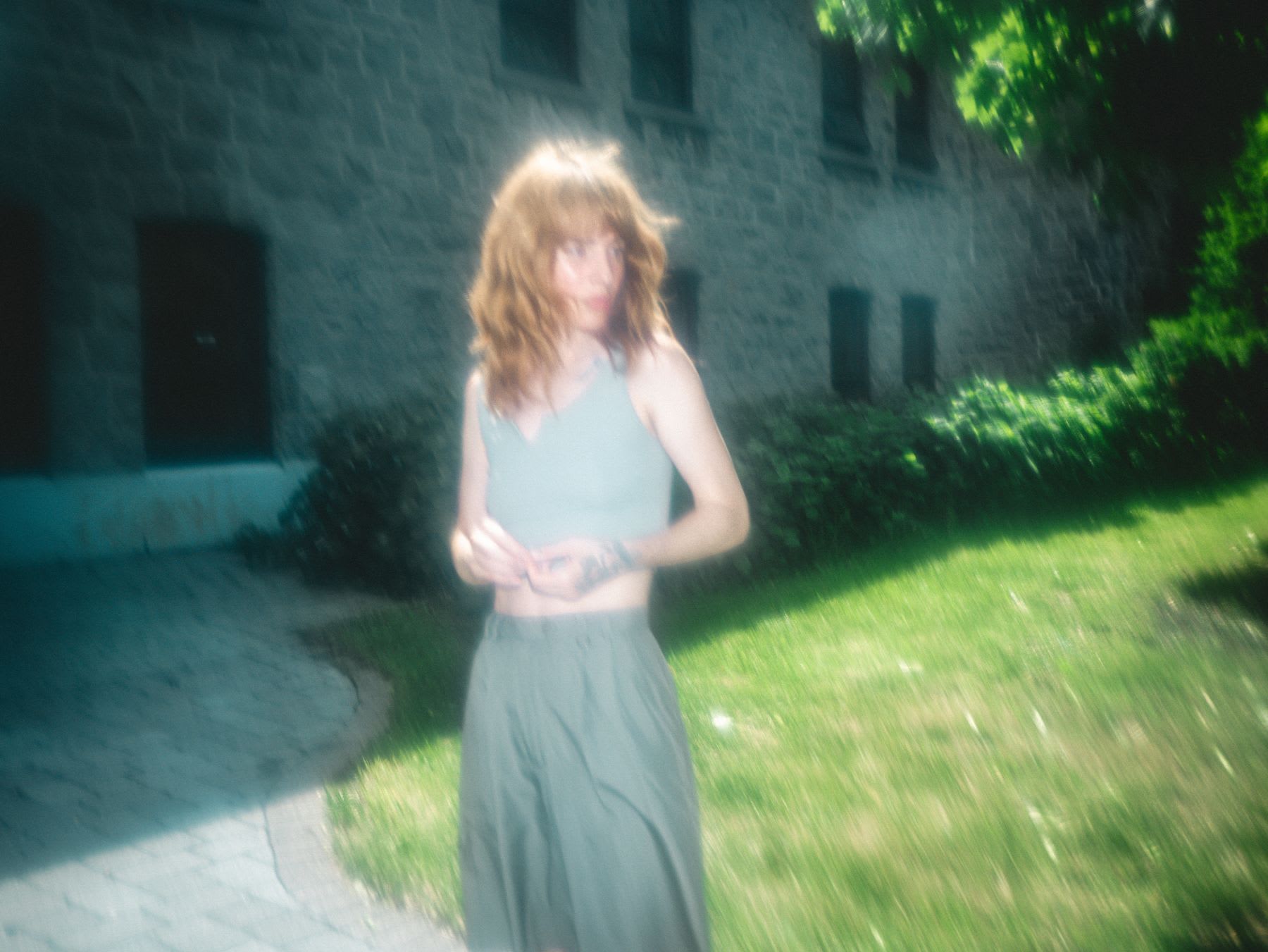 A portrait of a woman in gray clothes and yellow hair standing in a yard on a green lawn looking to the side