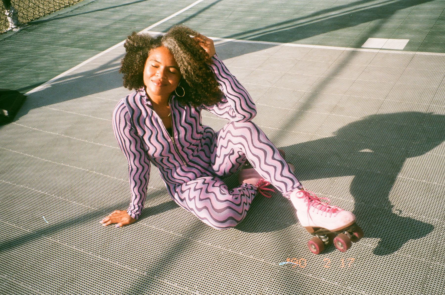 A young woman on rollerskates, smiling and posing while sitting on the floor