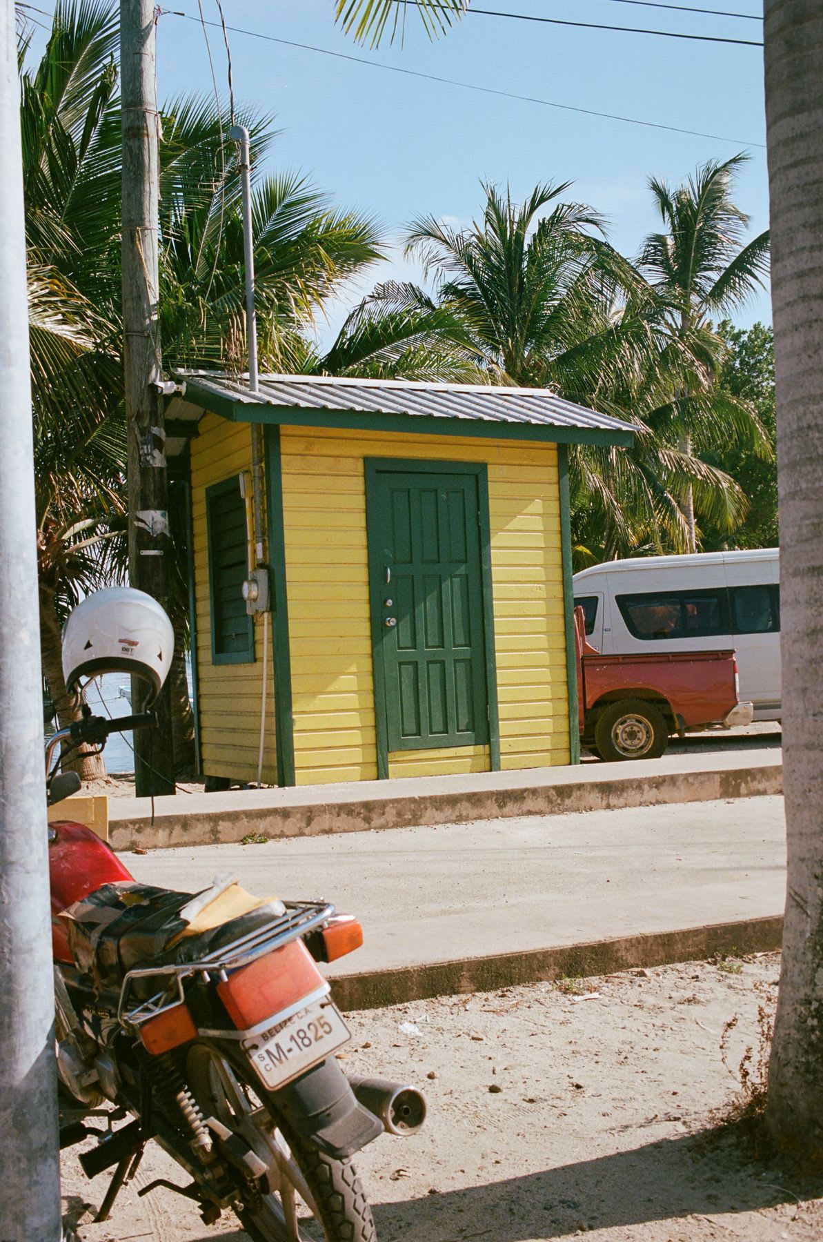 Bright yellow and green shed stands in an occupied parking lot near the street on a sunny day.