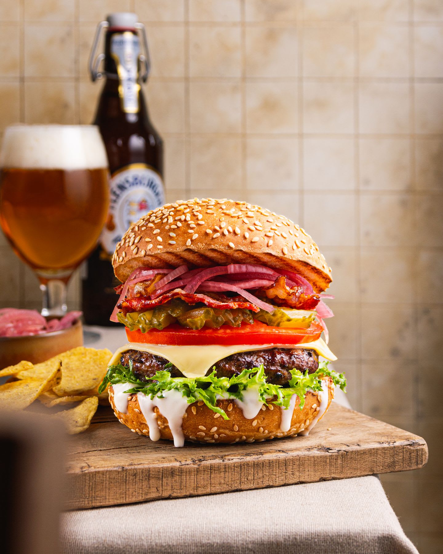 Stacked burger with the works on a table with a glass of beer and a bottle