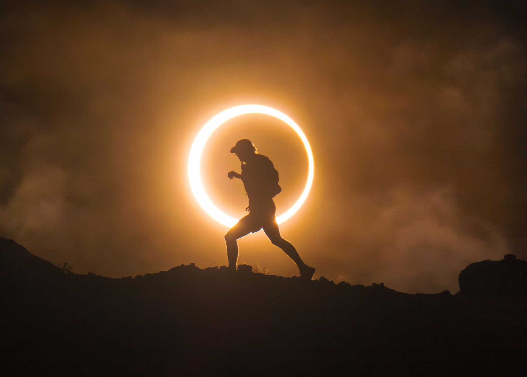 A silhouette of a man walking in front of a solar eclipse.