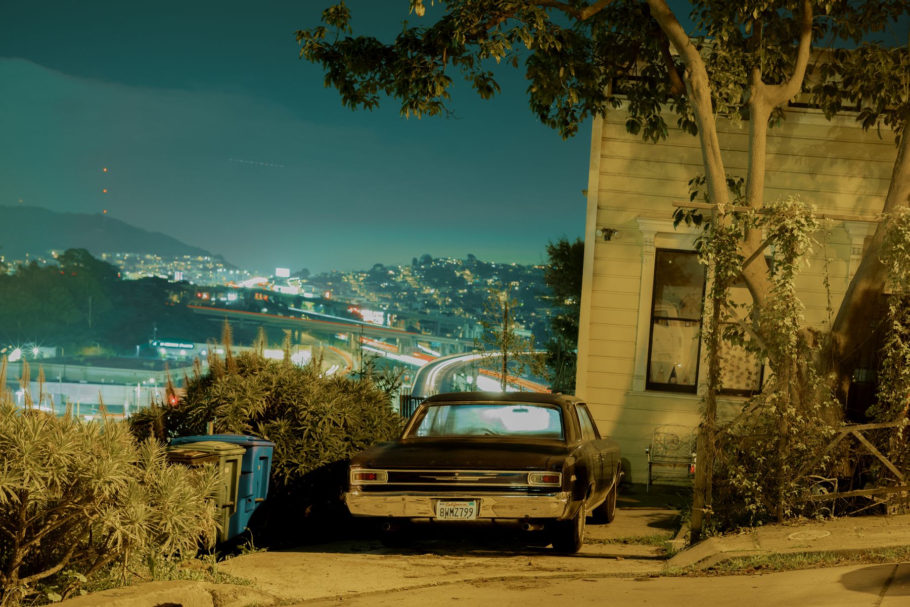 An antique car parked outside a house with a view of the city.