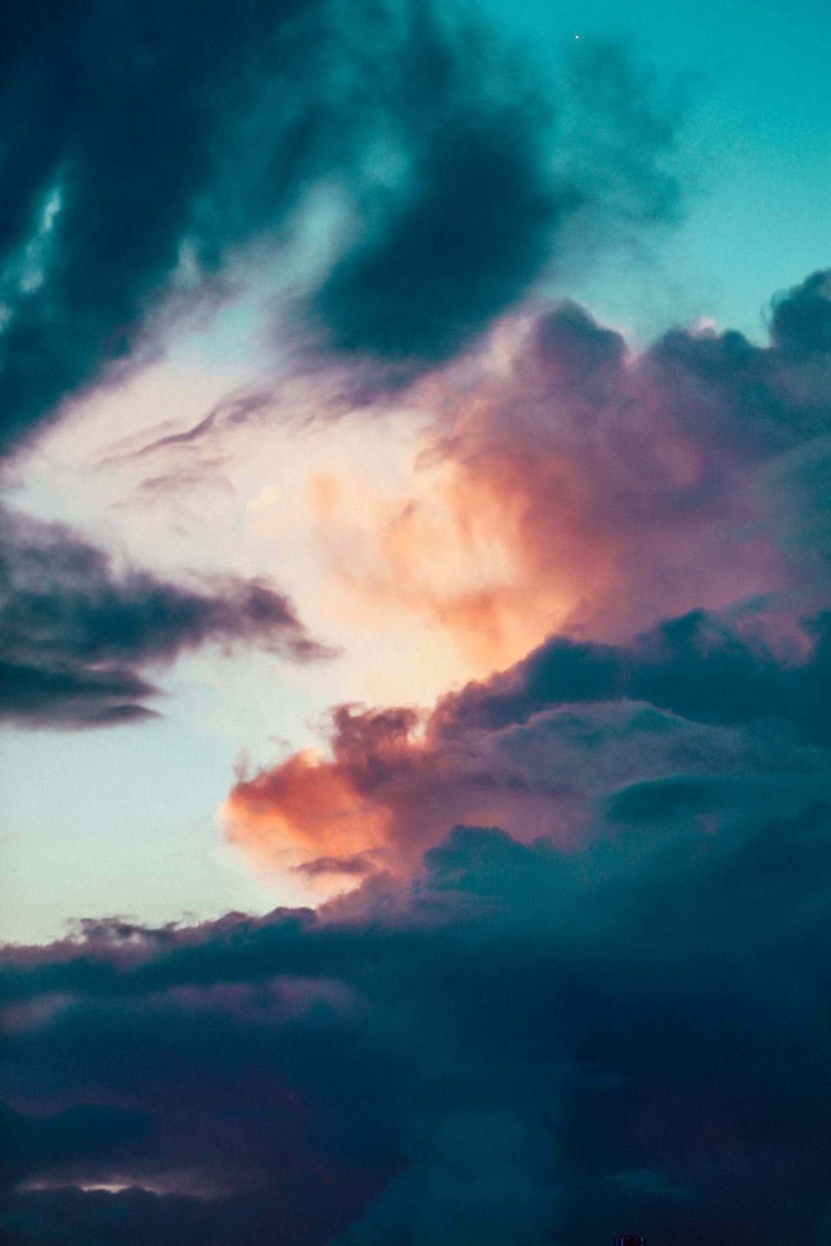 Dramatic teal and orange cumulus clouds create a moody and abstract skyscape during dusk.