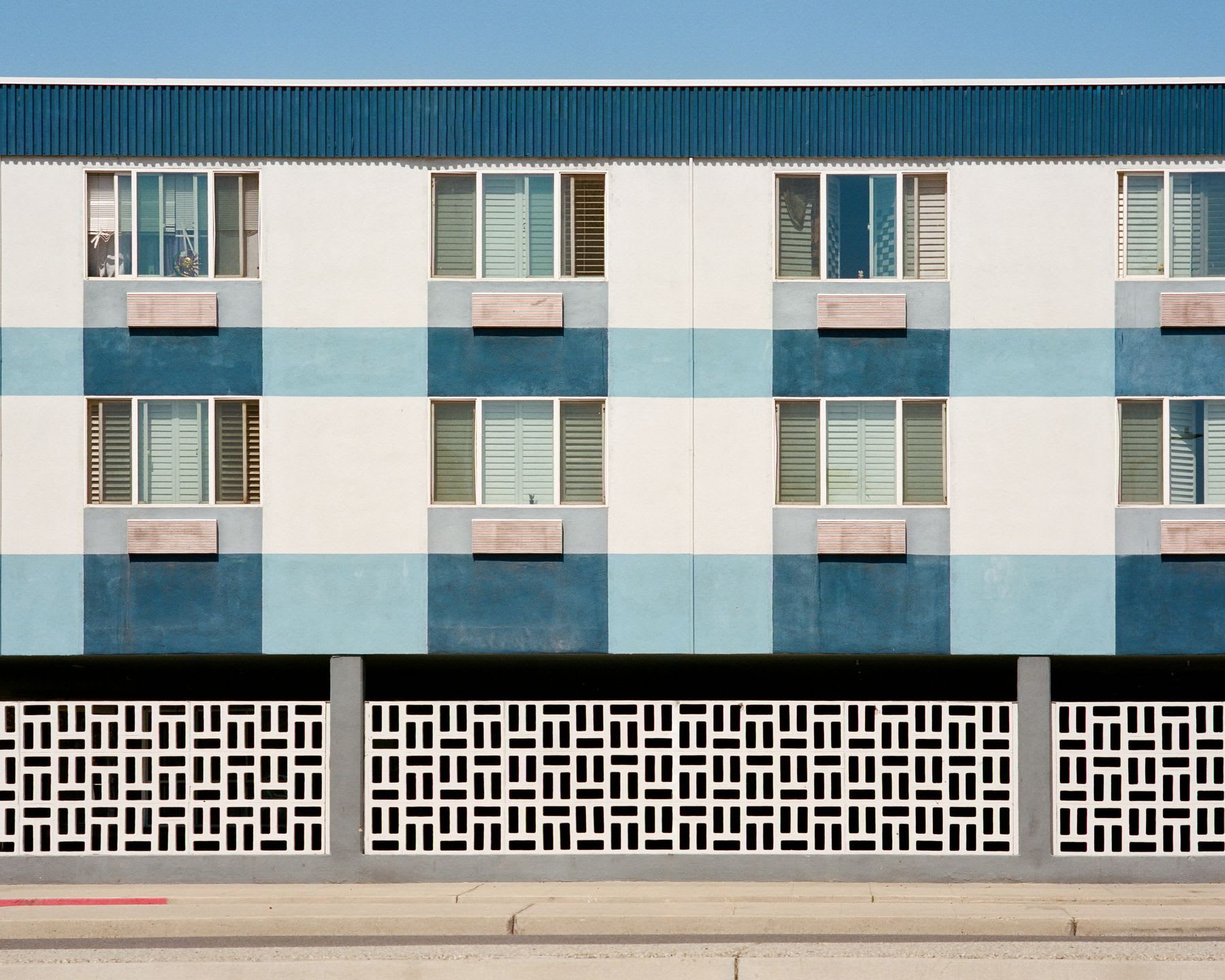 The geometric facade of a blue and white painted building with a decorative concrete screen wall under a clear blue sky.