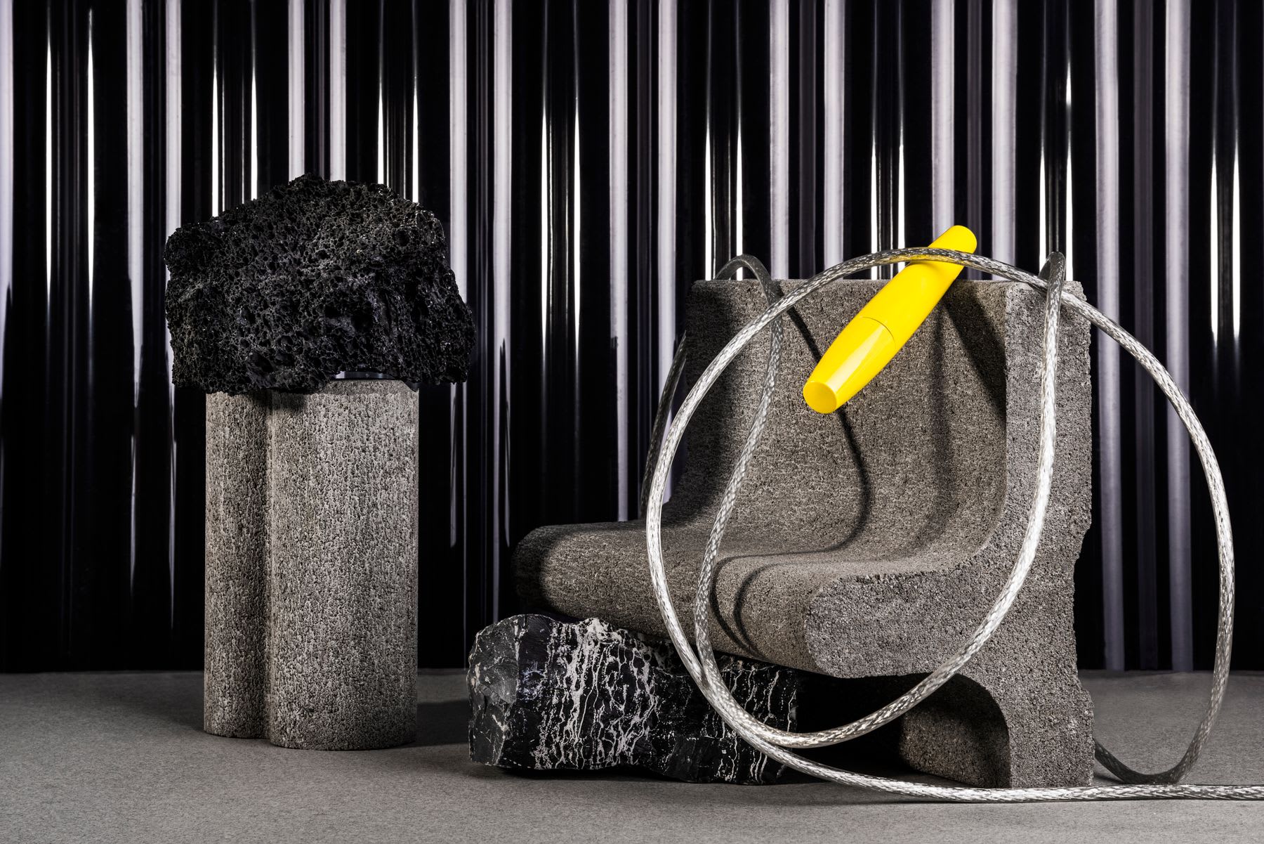 a scene where a cement bench is wrapped with a long metal cable near a black and white marble rock.