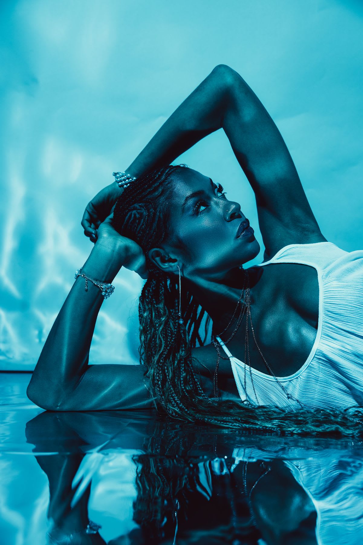 Female model lying on a reflective floor with her hands on her head and wearing a white top