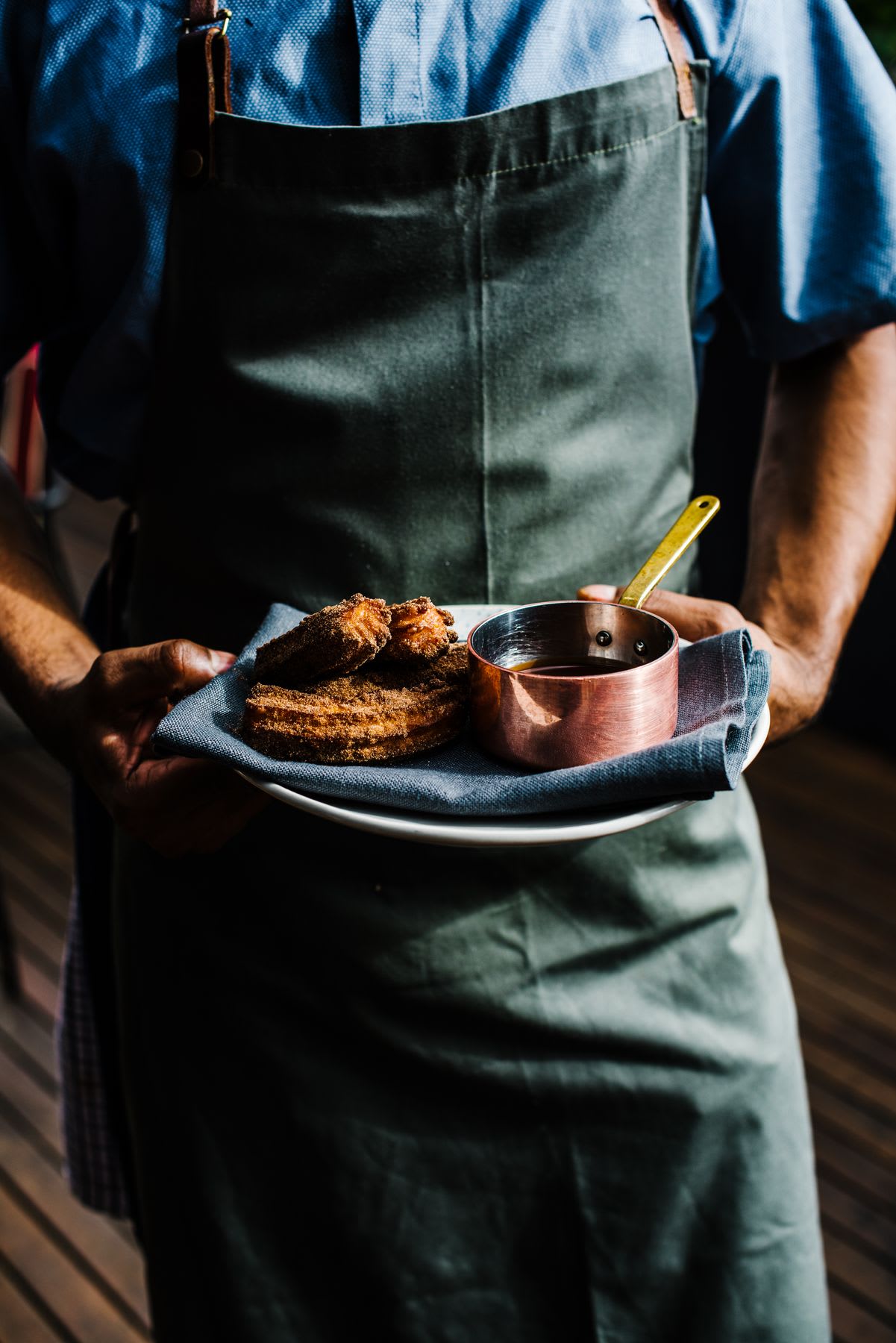 Person wearing apron holds plate of churros and sauce