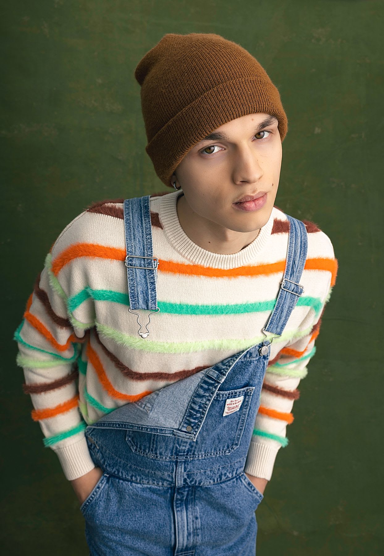Man with a brown cap wearing denim overalls with his hands in his pockets
