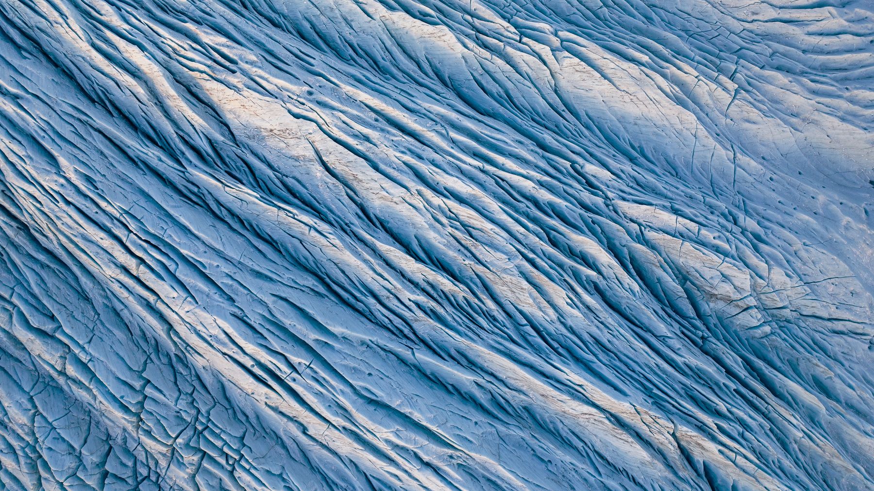 A colossal ice sheet fractured with deep, snaking crevasses stretches across the snowy landscape.