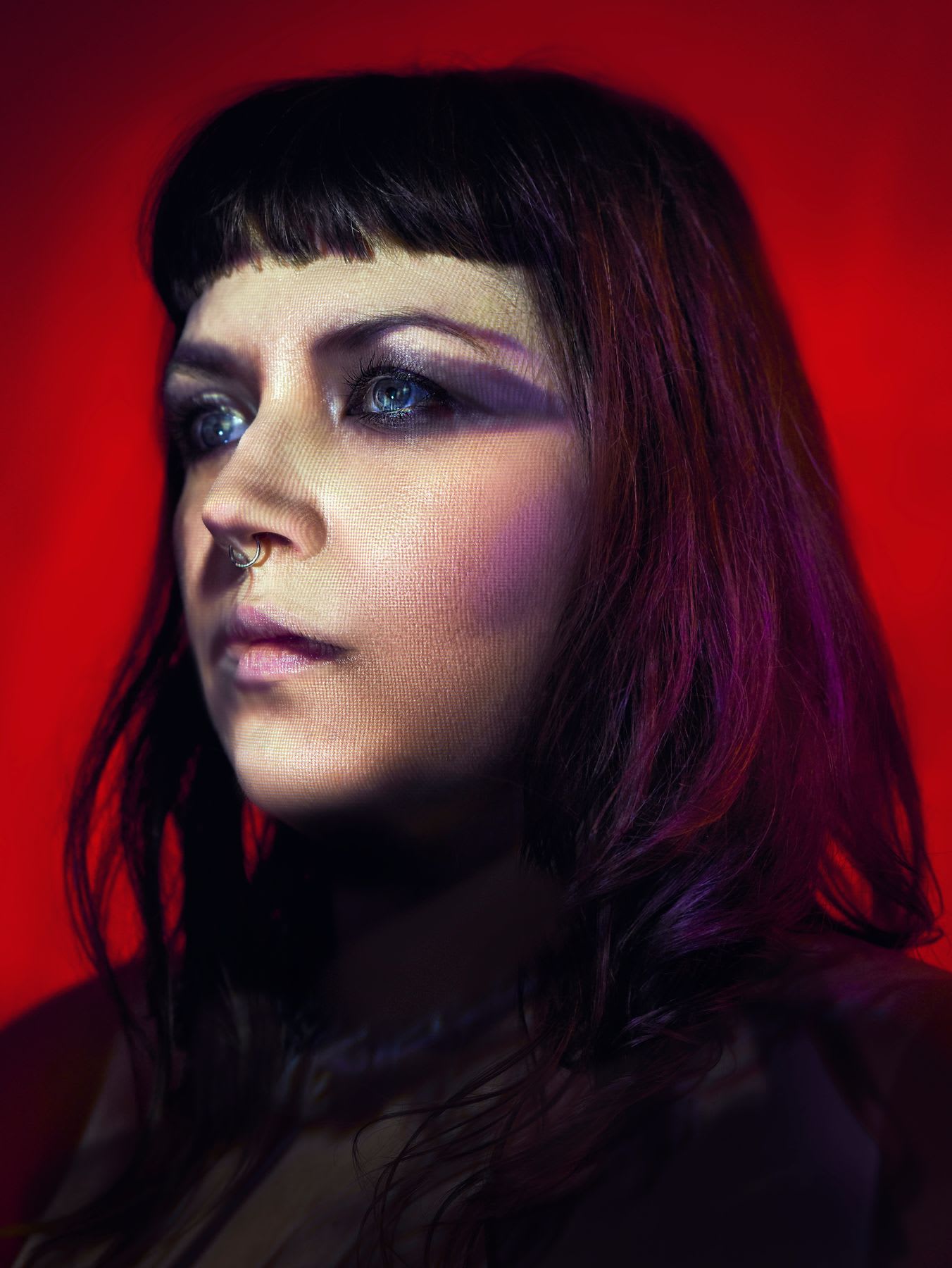 A young woman wearing purple makeup poses in front of a red background.