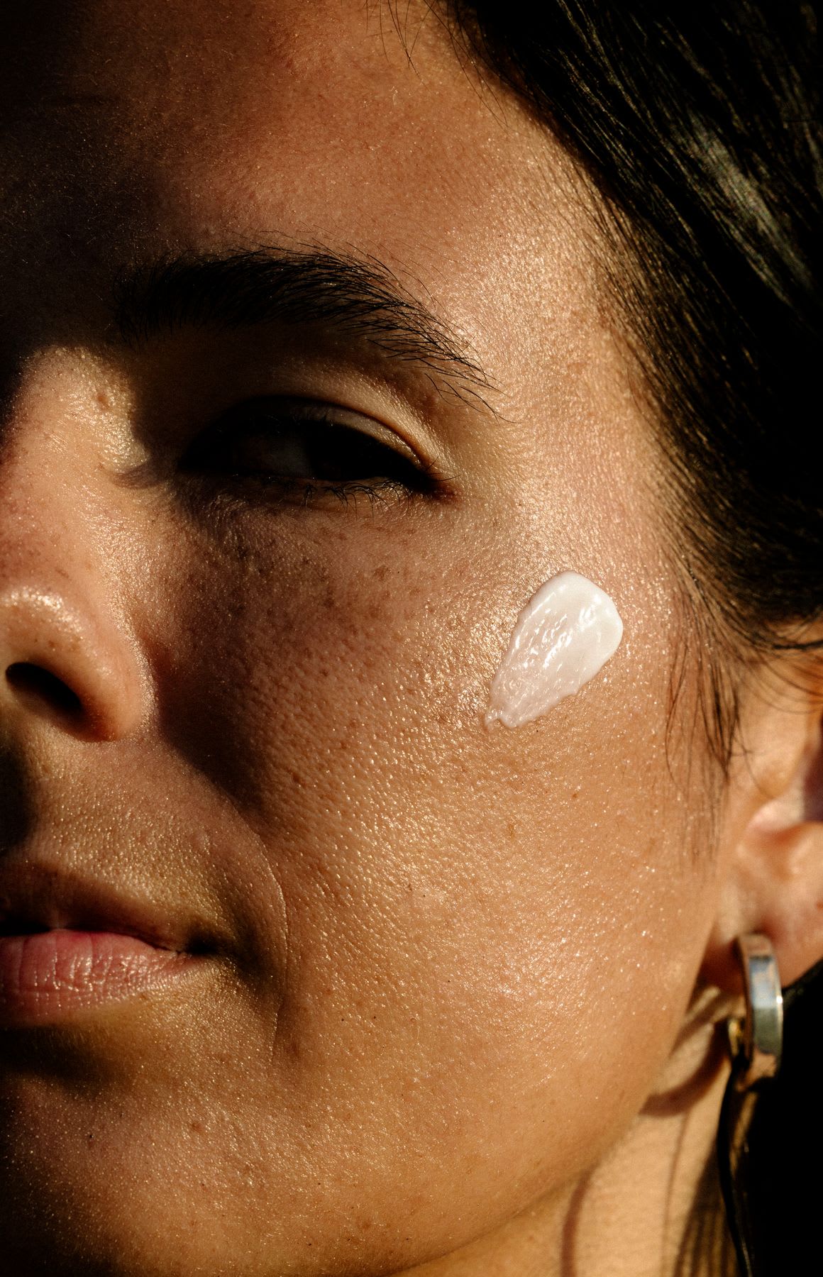 Closeup of a woman with lotion on her cheek as she looks out the corner of her eye.