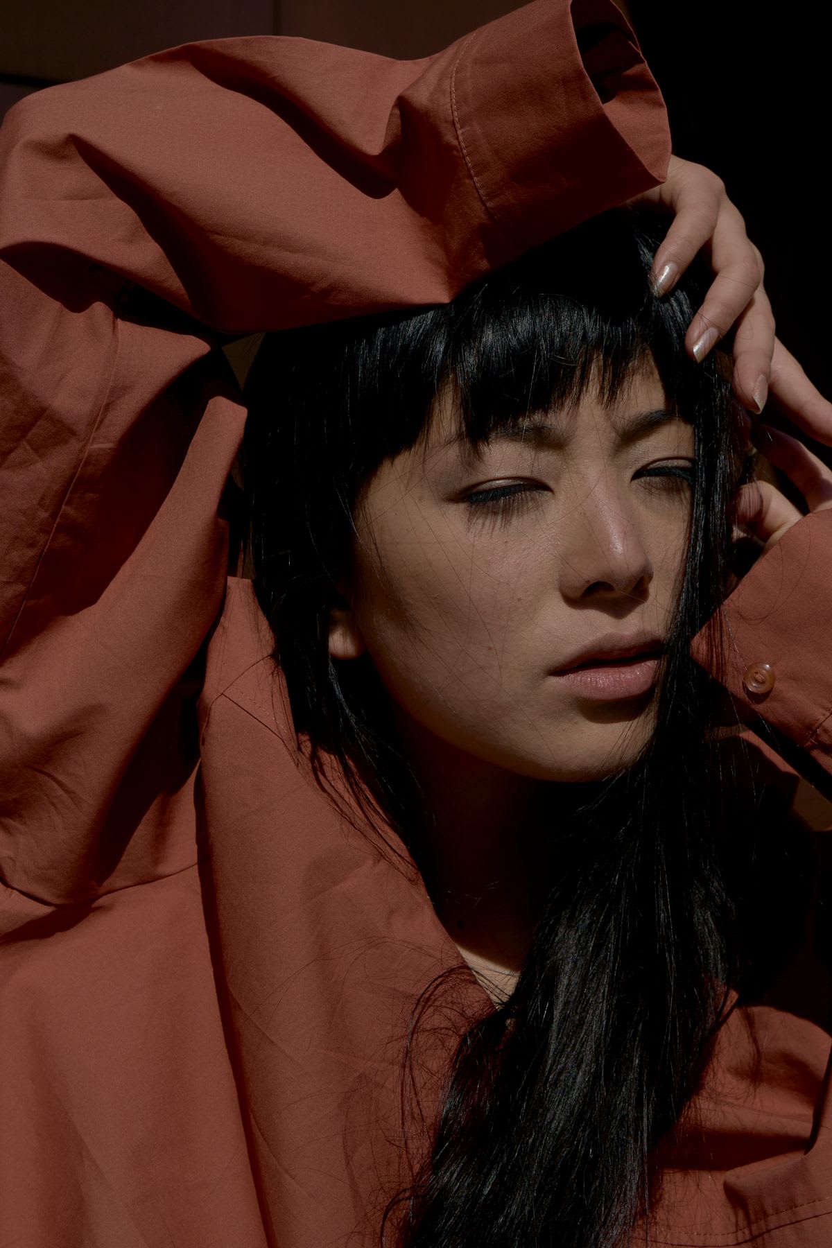 Portrait of an Asian woman wearing a long sleeve dark orange shirt.