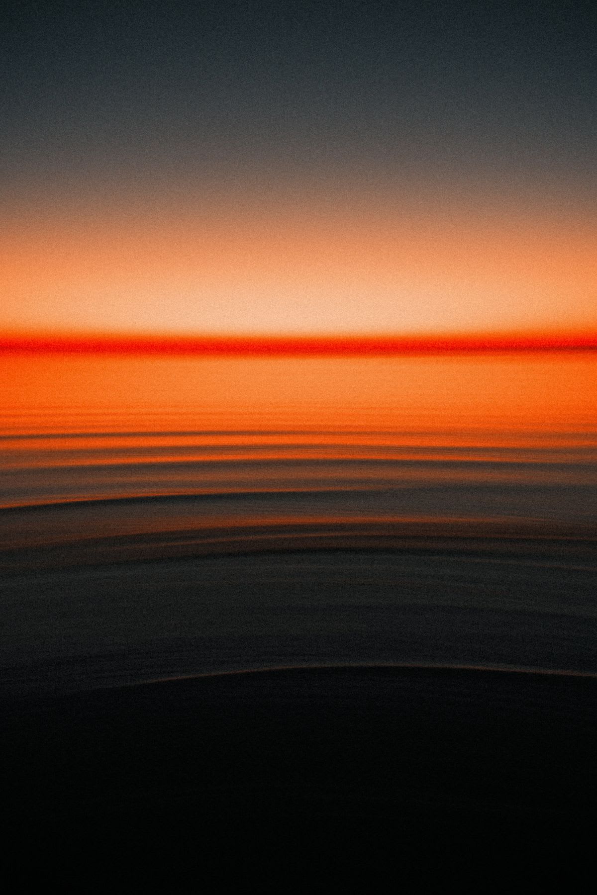 An abstract, motion-blurred photograph captures the vibrant orange and red hues of a sunset over a dark sea.