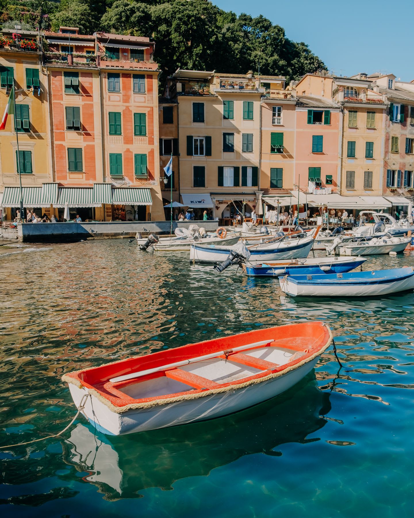 A group of rowboats are parked on a Venetian canal with orange buildings nearby.