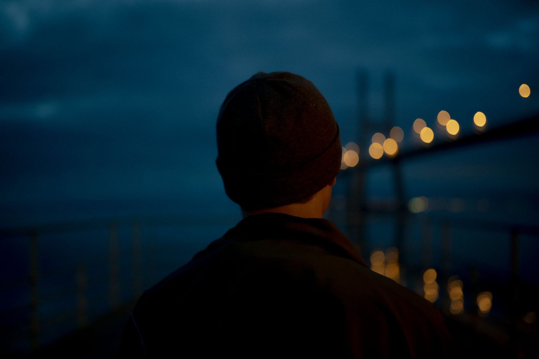 The back of a man's neck that is wearing a black cap and looking forward and in a place where it is getting dark