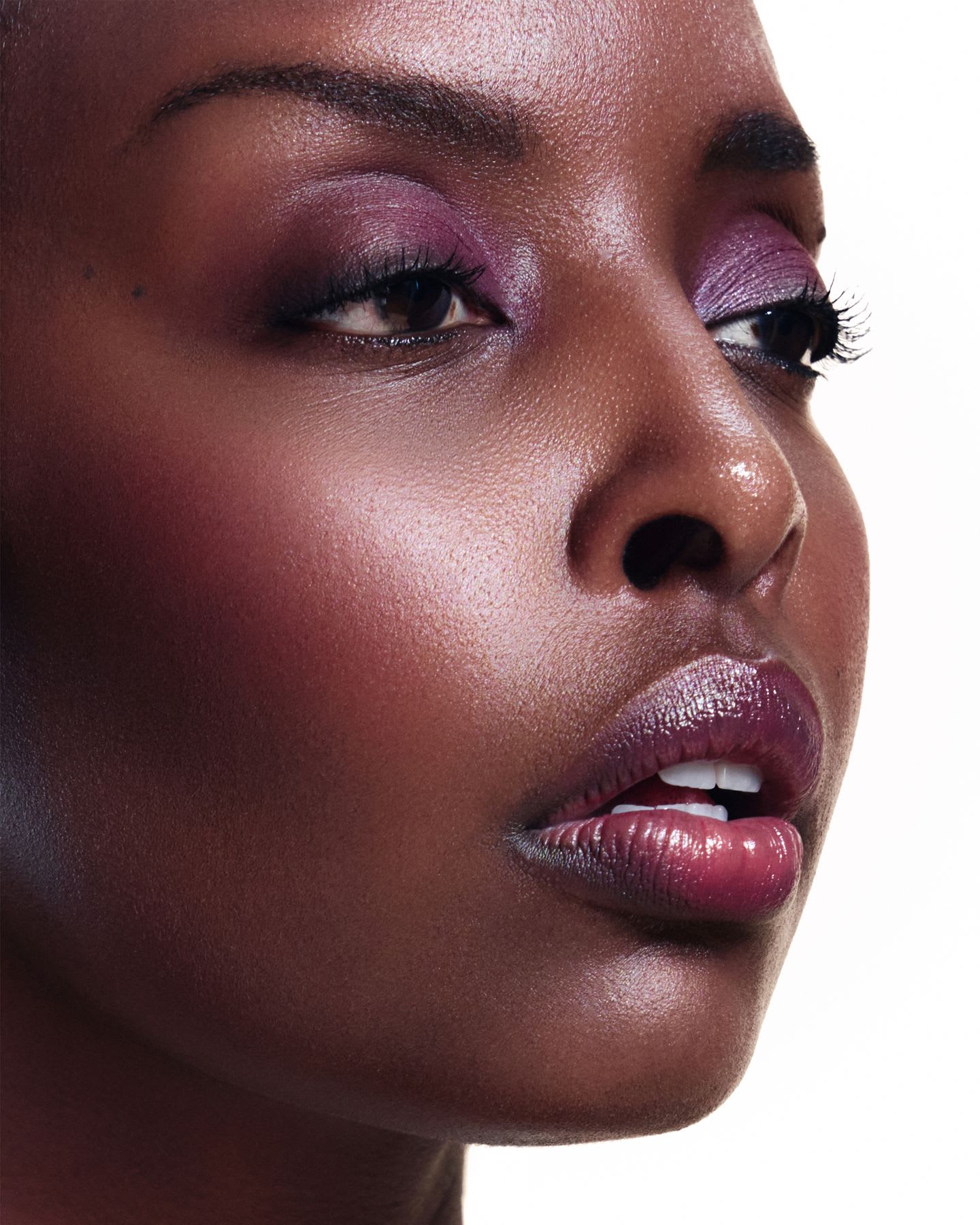 A woman looking to the side with purple eye shadow and mauve lipstick.