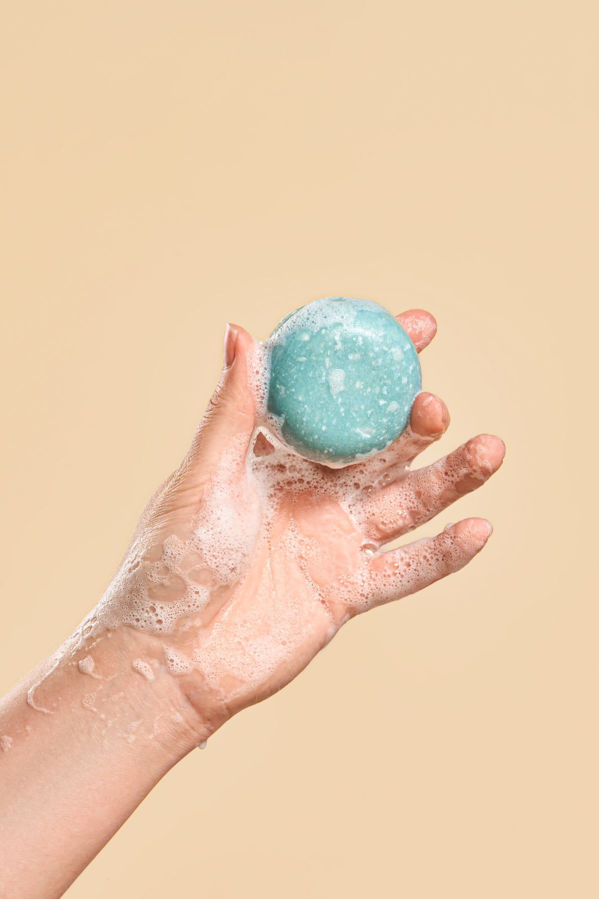 a woman’s hand holds a round, turquoise-colored bar of soap, creating a lather of bubbles.
