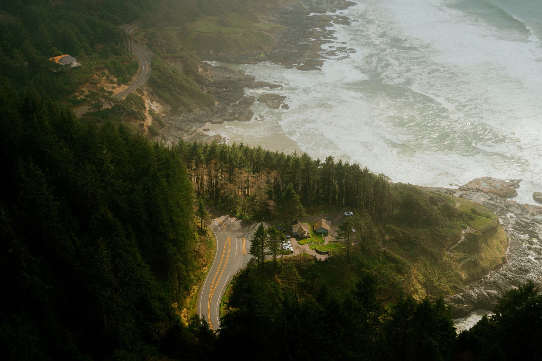 An aerial view reveals a charming coastal town ablaze with autumnal hues, where the turquoise waves gently caress the shore and a colorful mosaic of parked cars dot the landscape.