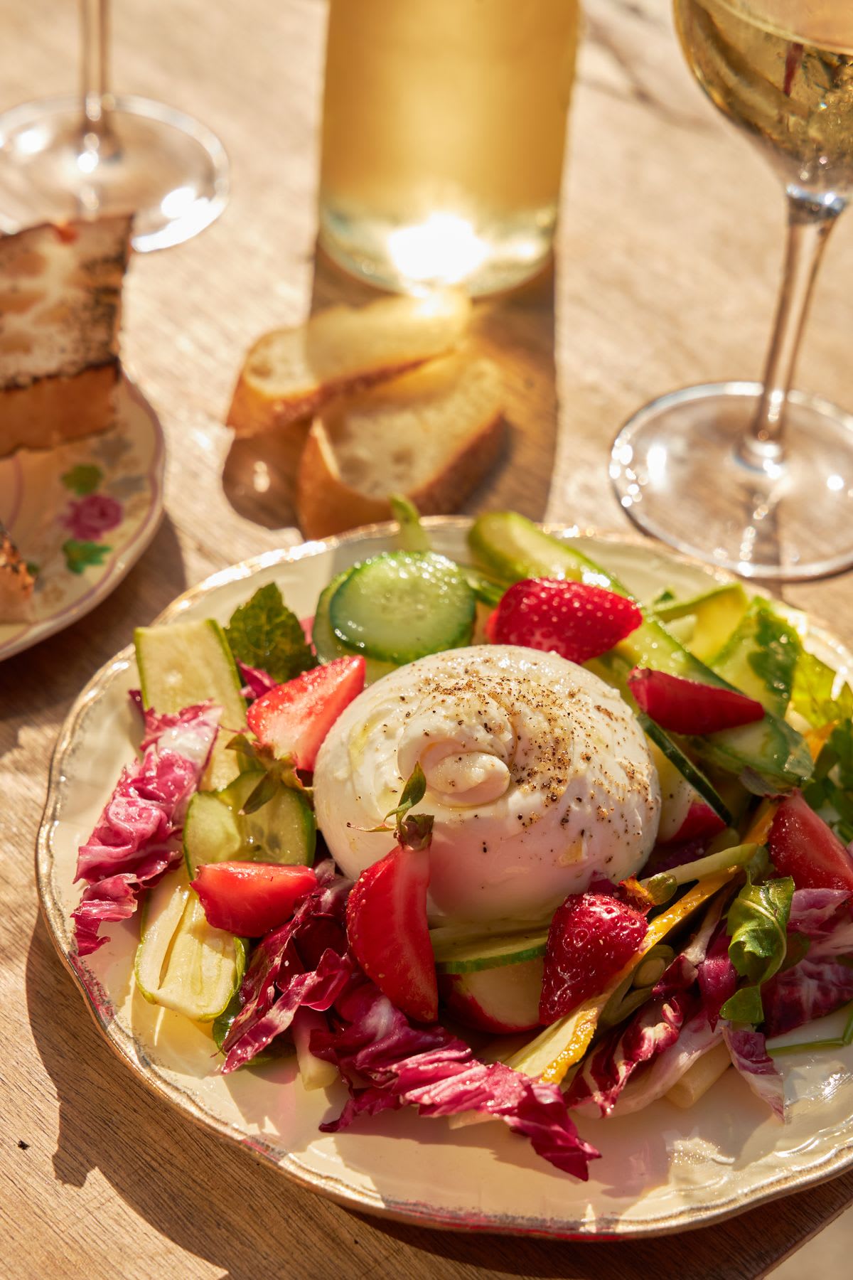 A round white plate with a creamy burrata cheese sits on a wooden table next to a glass of white wine.